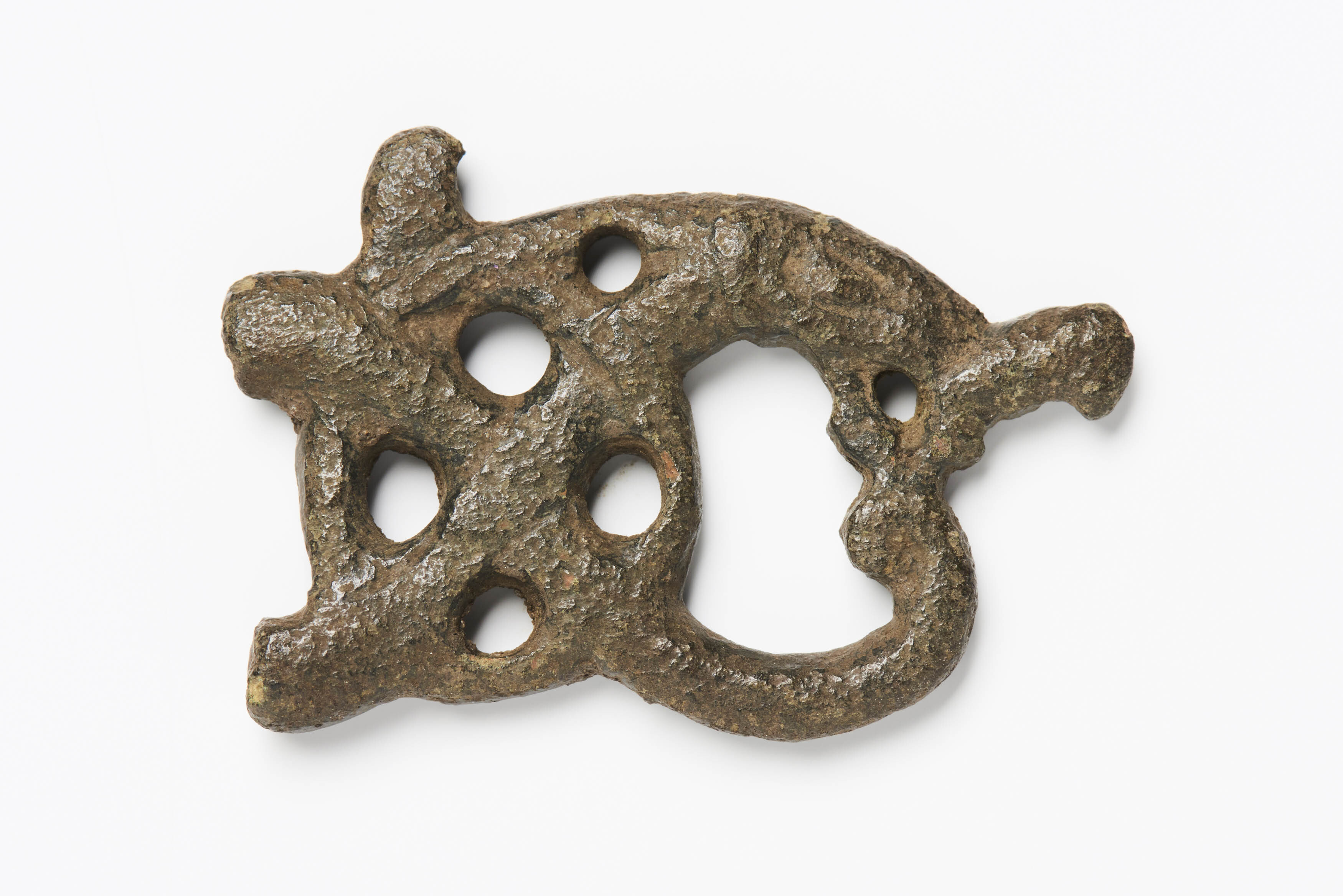 A small metal object of asymmetrical shape and snake-like lines, with six circular holes pierced through.