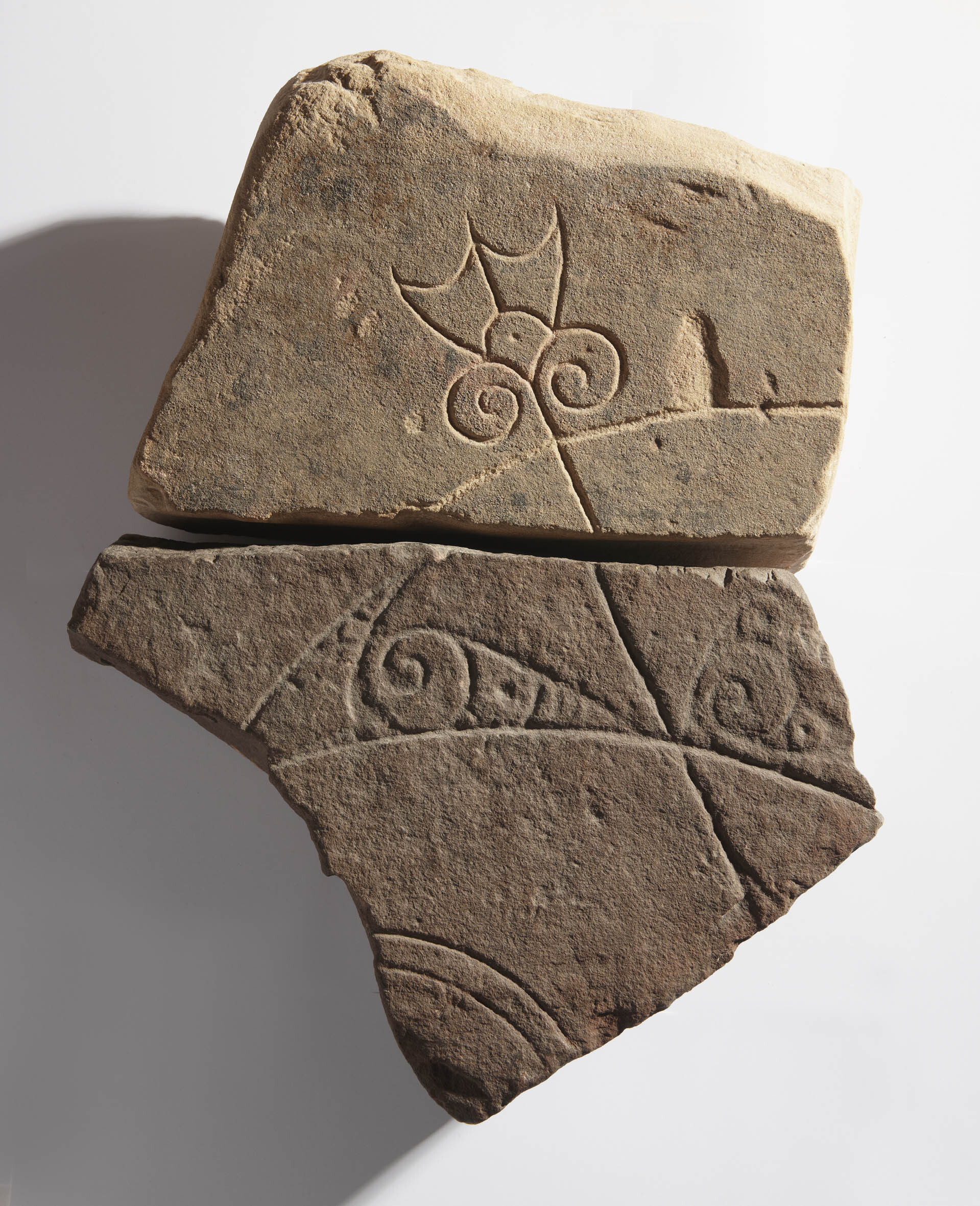 Two fragments from a Pictish symbol stone.  The lower fragment is a real stone and the upper fragment is a fibreglass replica of the real stone which is held at Dunrobin Museum.  The fragments join together to show part of a 'crescent and V-rod' Pictish symbol.