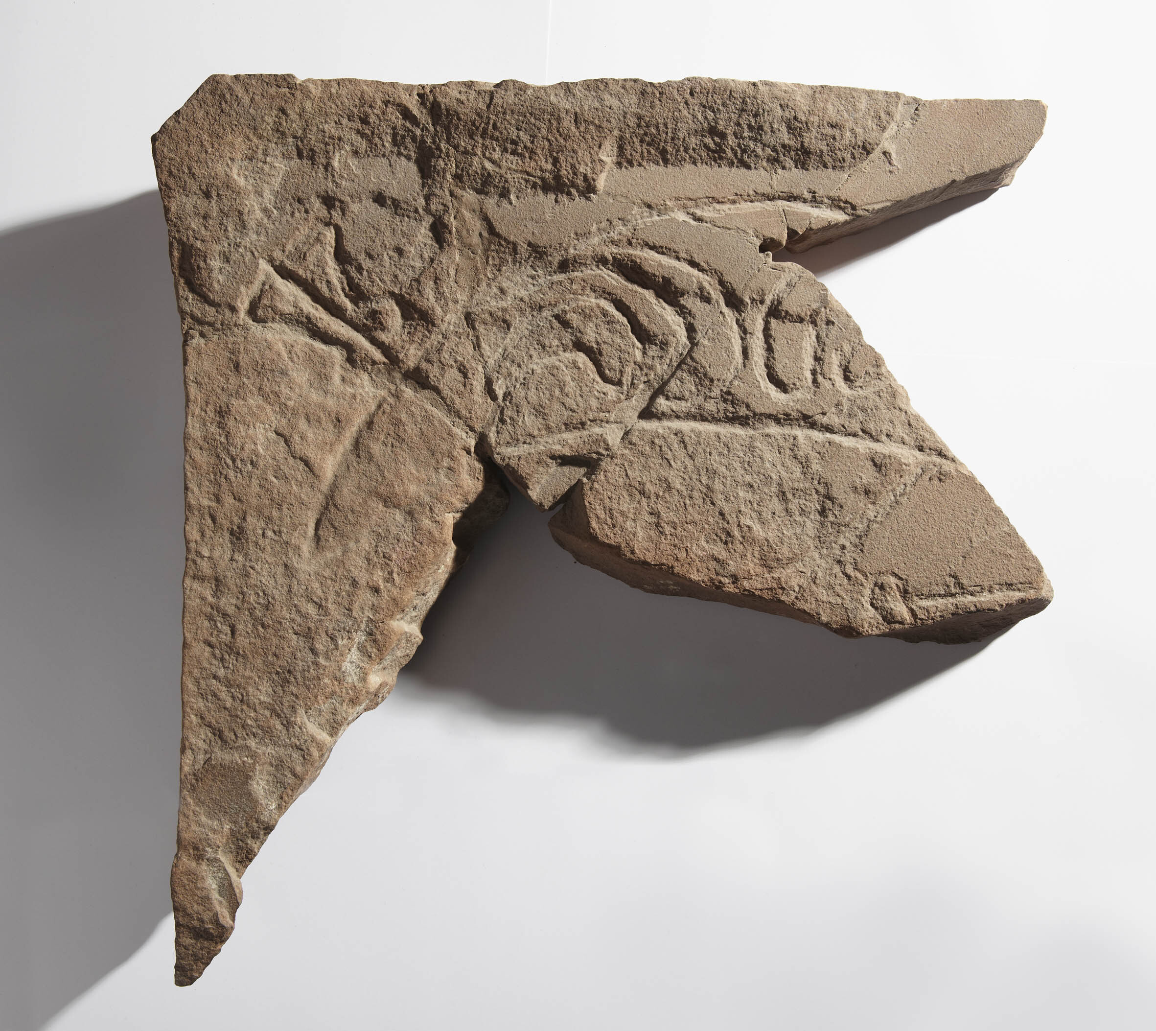 Fragment of a Pictish symbol stone.  The stone is approximately arrow-shaped and shows half of a 'crescent and V-rod' Pictish symbol carved into stone.