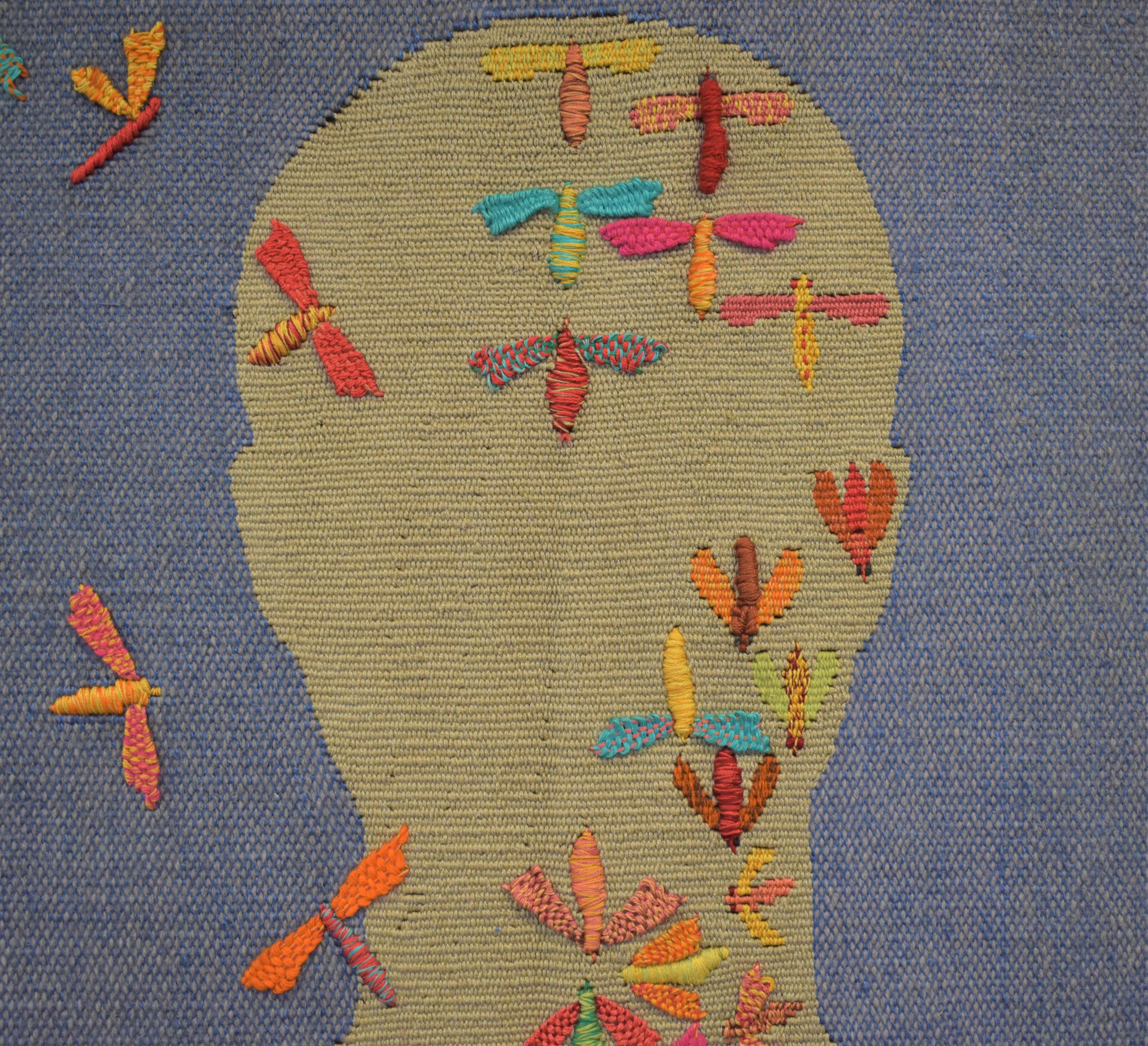 Close-up view of the central head from Man and the Enironment tapestry by Fiona Mathison. A cream head against a blue sky with colourful insects contained within the outline of the head.