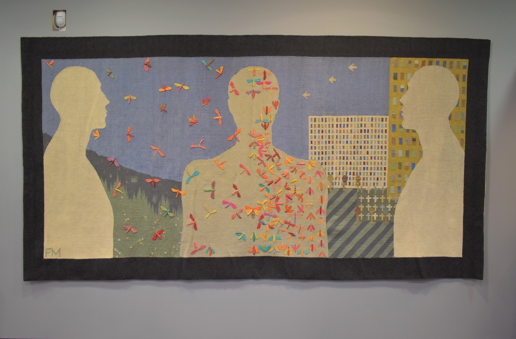 A large, long rectangular tapestry with three silhouette figures in cream.  The figure on the left faces into the middle and has a background of nature, while the figure on the right also faces into the middle but has a background of buildings.  The figure in the middle is face on.  On the nature side the sky is full of colourful flying insects.  On the urban side, the insects are crammed into the central figure's silhouette.  There is a thick black border around the edge.