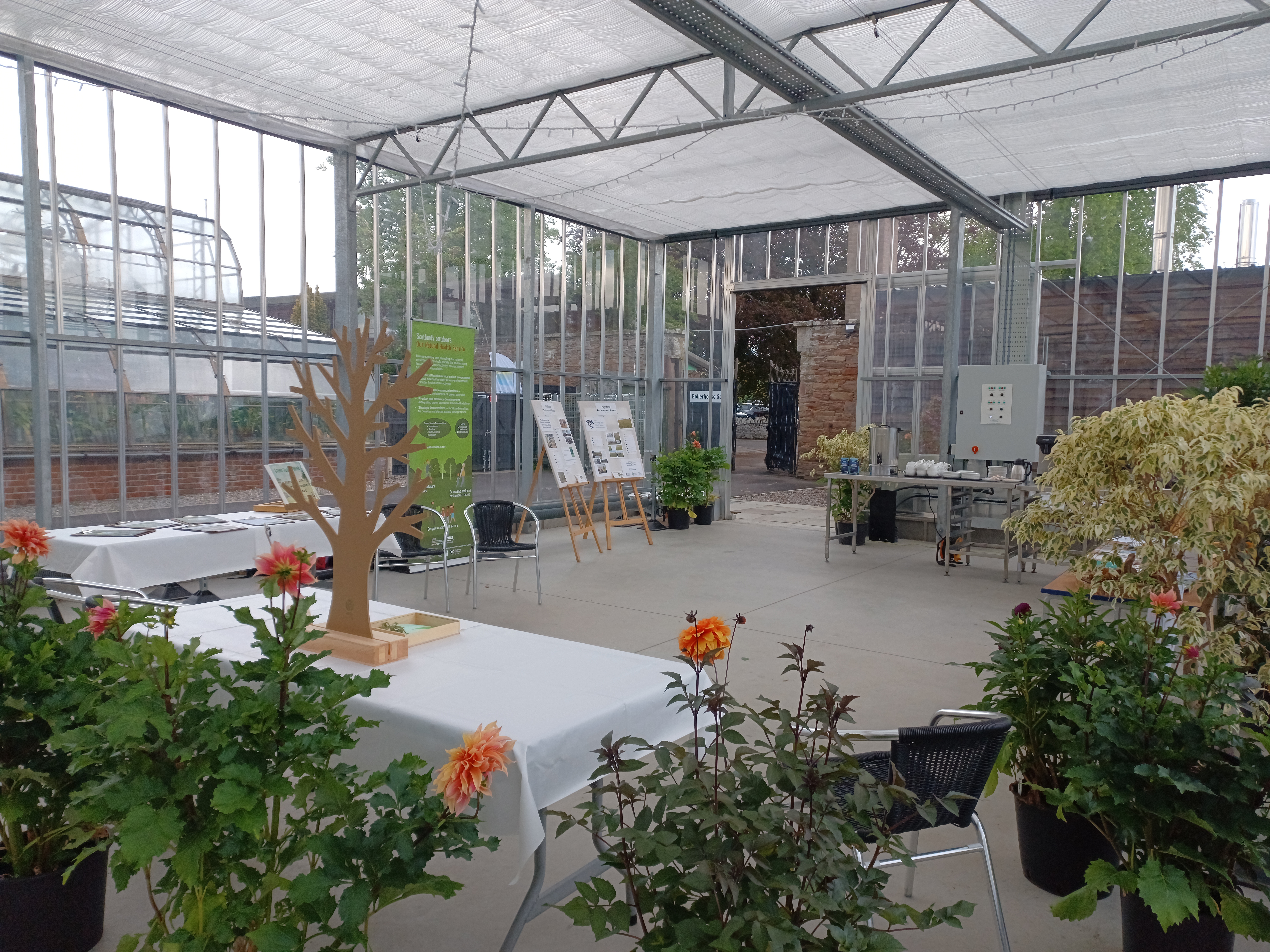 A bright and airy glasshouse space with tables and stands set up for an event.