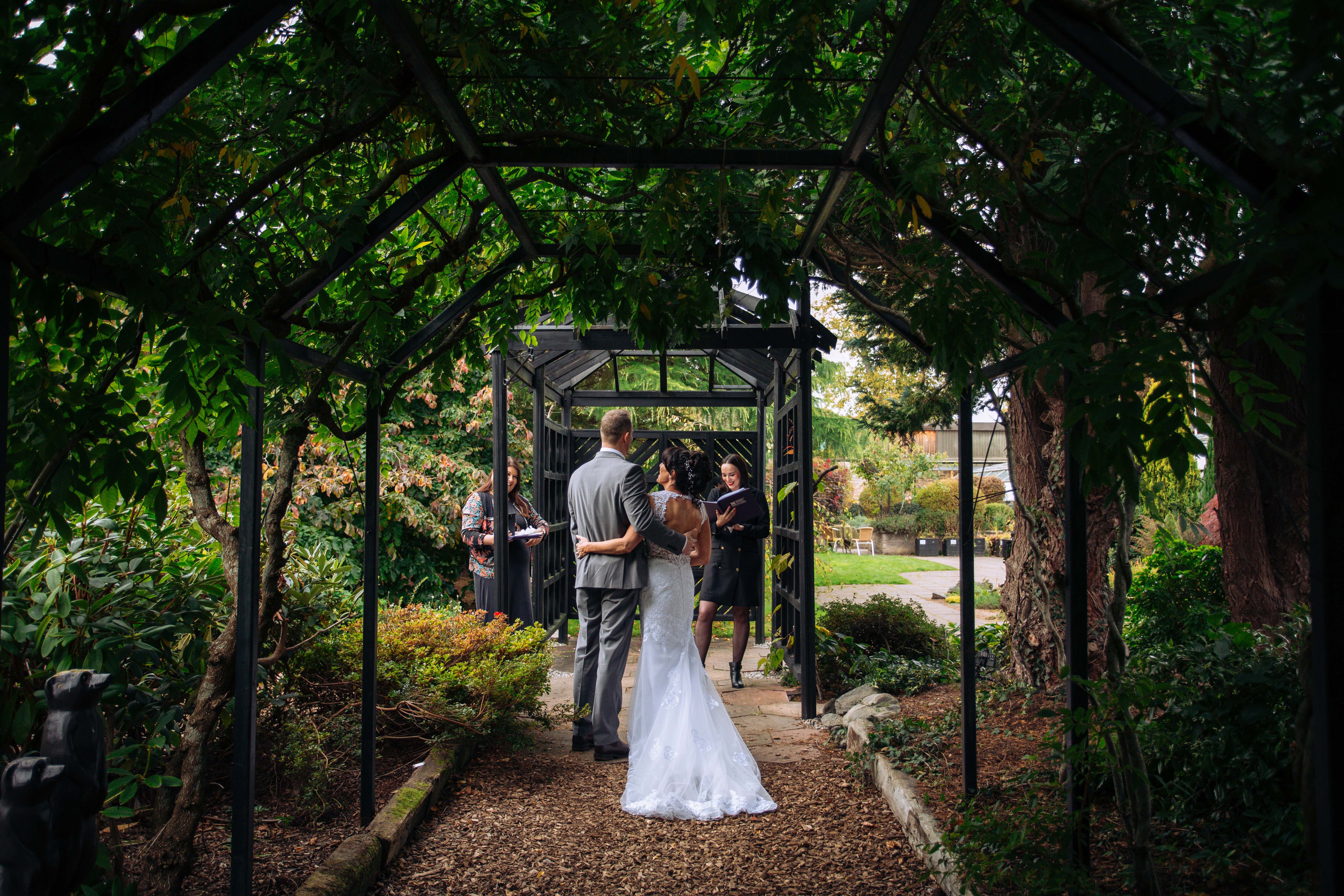 Luscious greenery overhanging a pergola, with a bride and groom in the centre.