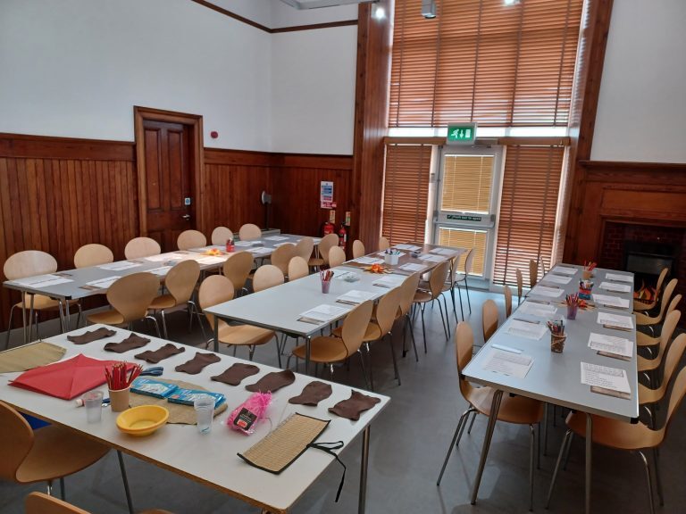 Room with tables and chairs set up for a craft activity, with paper, pencils, and materials laid out.