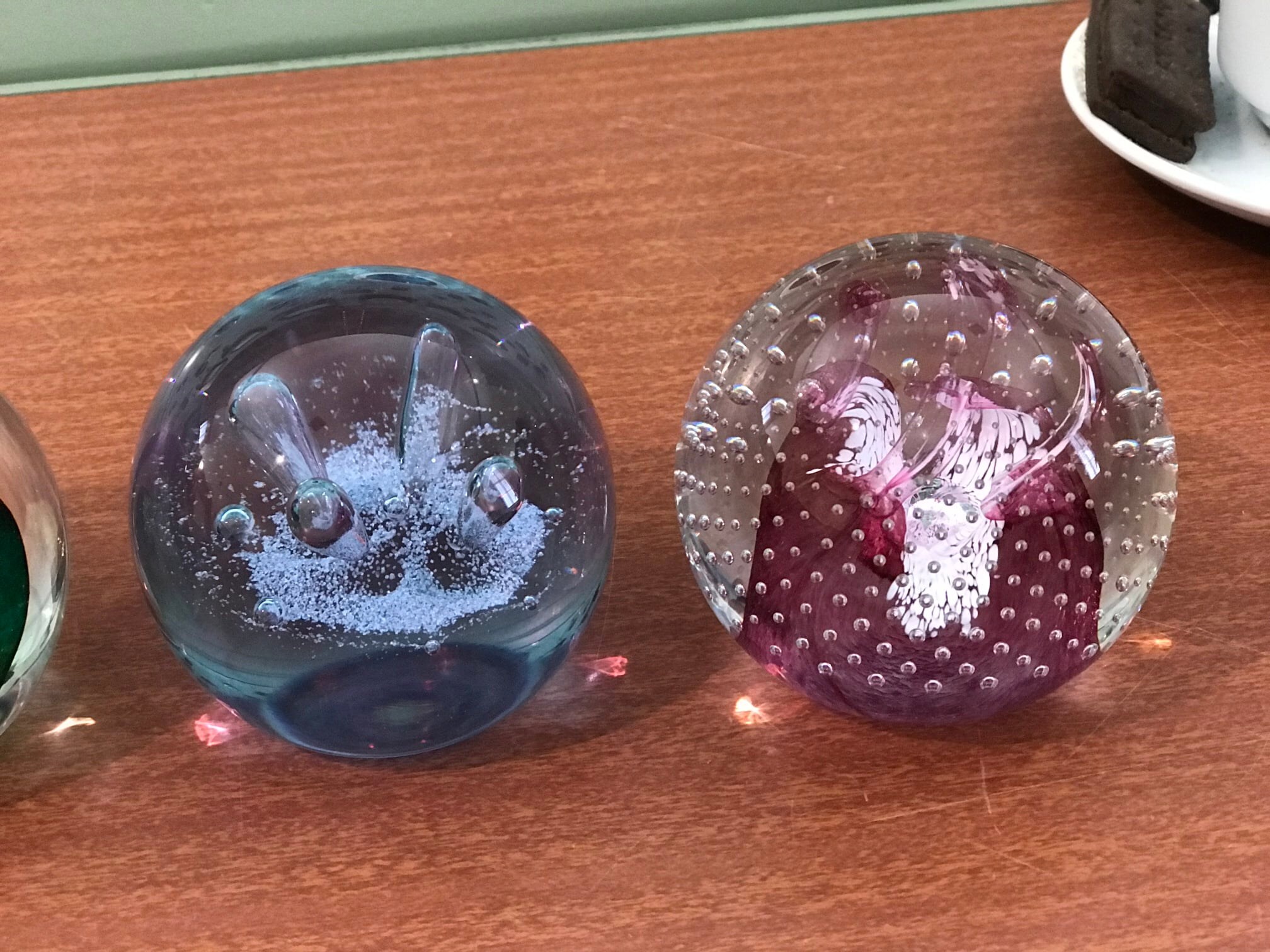 Two decorative glass paperweights with blue and pink designs and bubble patterns on a wooden surface.