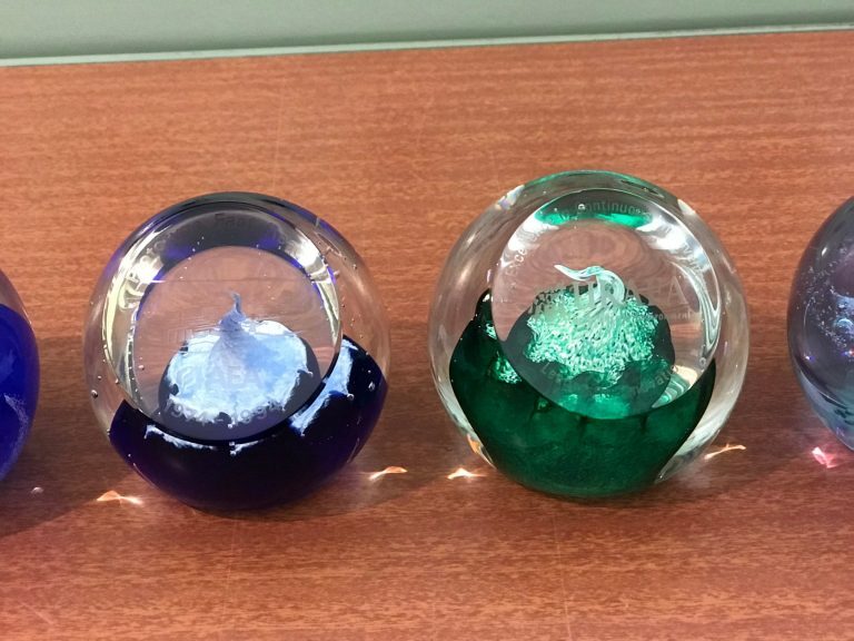 Two decorative glass paperweights with blue and green designs on a wooden surface.