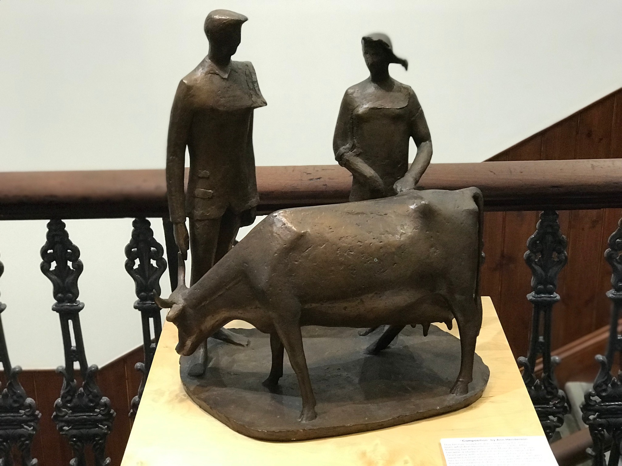 Bronze sculpture titled “Composition” by Ann Henderson, depicting two standing figures and a cow on a base.