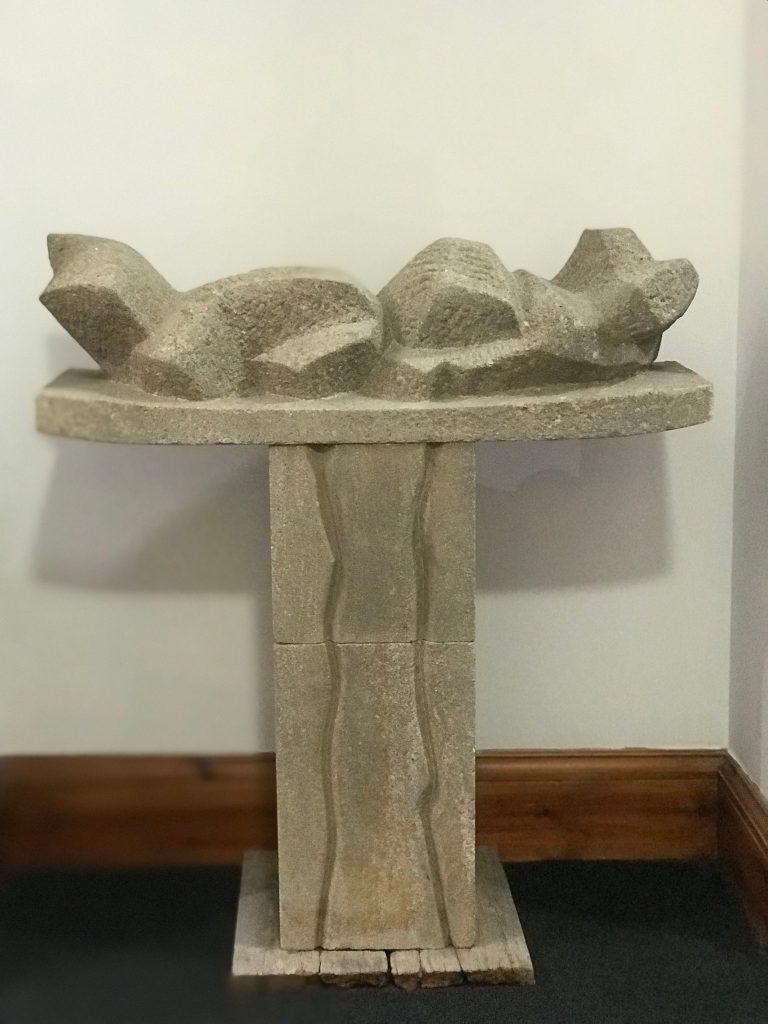 Abstract stone sculpture titled “Stone Form” by Ann Henderson, displayed on a pedestal against a wall.