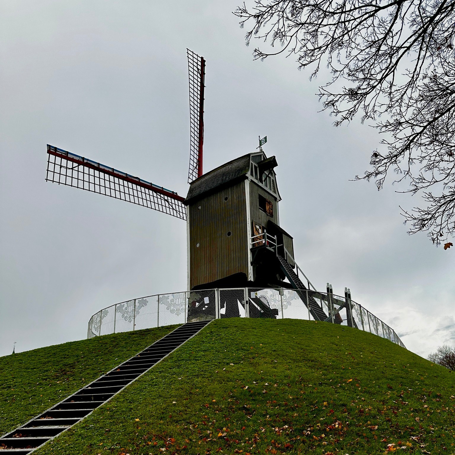A wooden windmill standing on a grassy hill under a cloudy sky.