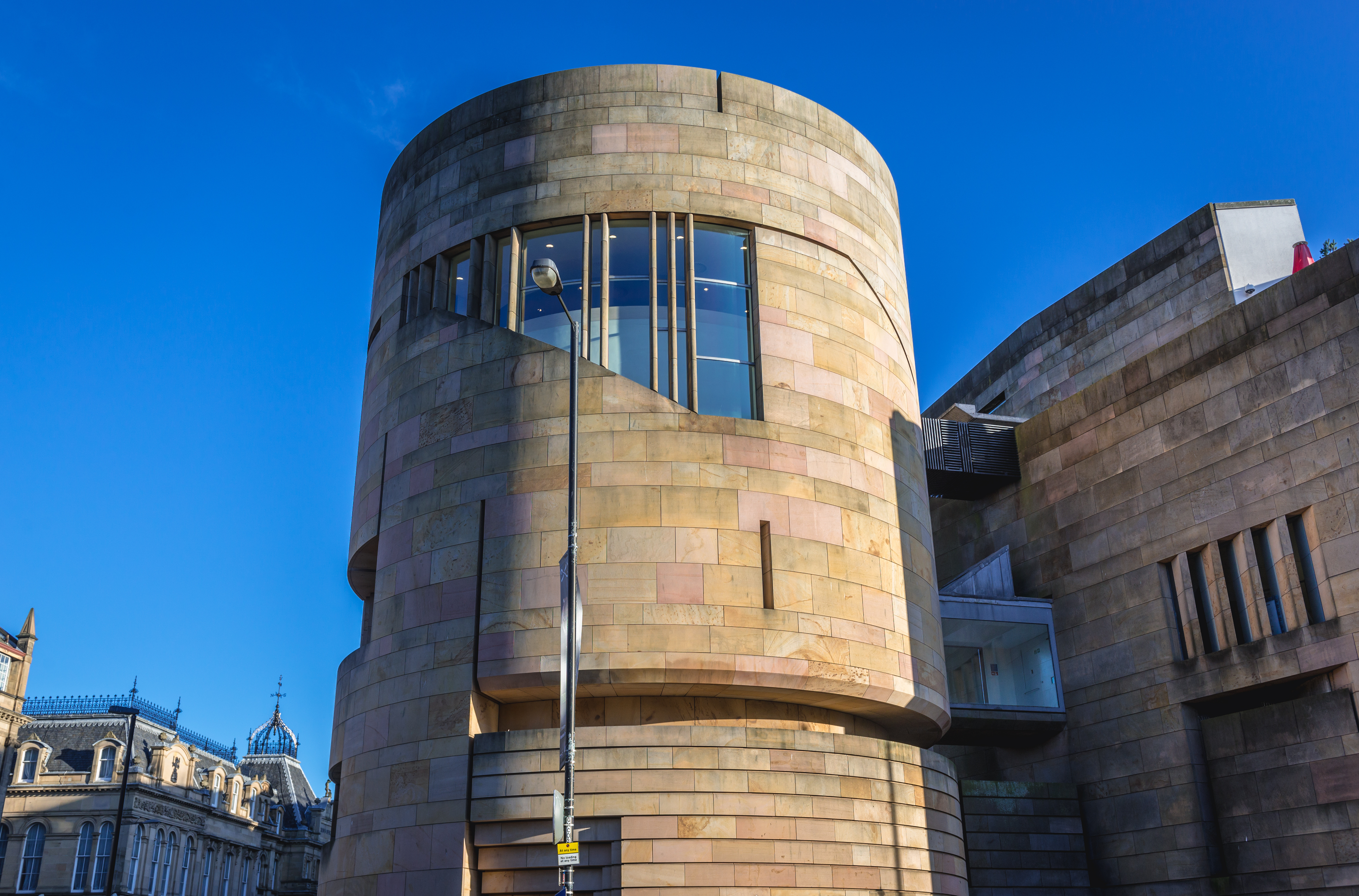 A modern stone building with curved walls against a blue sky.