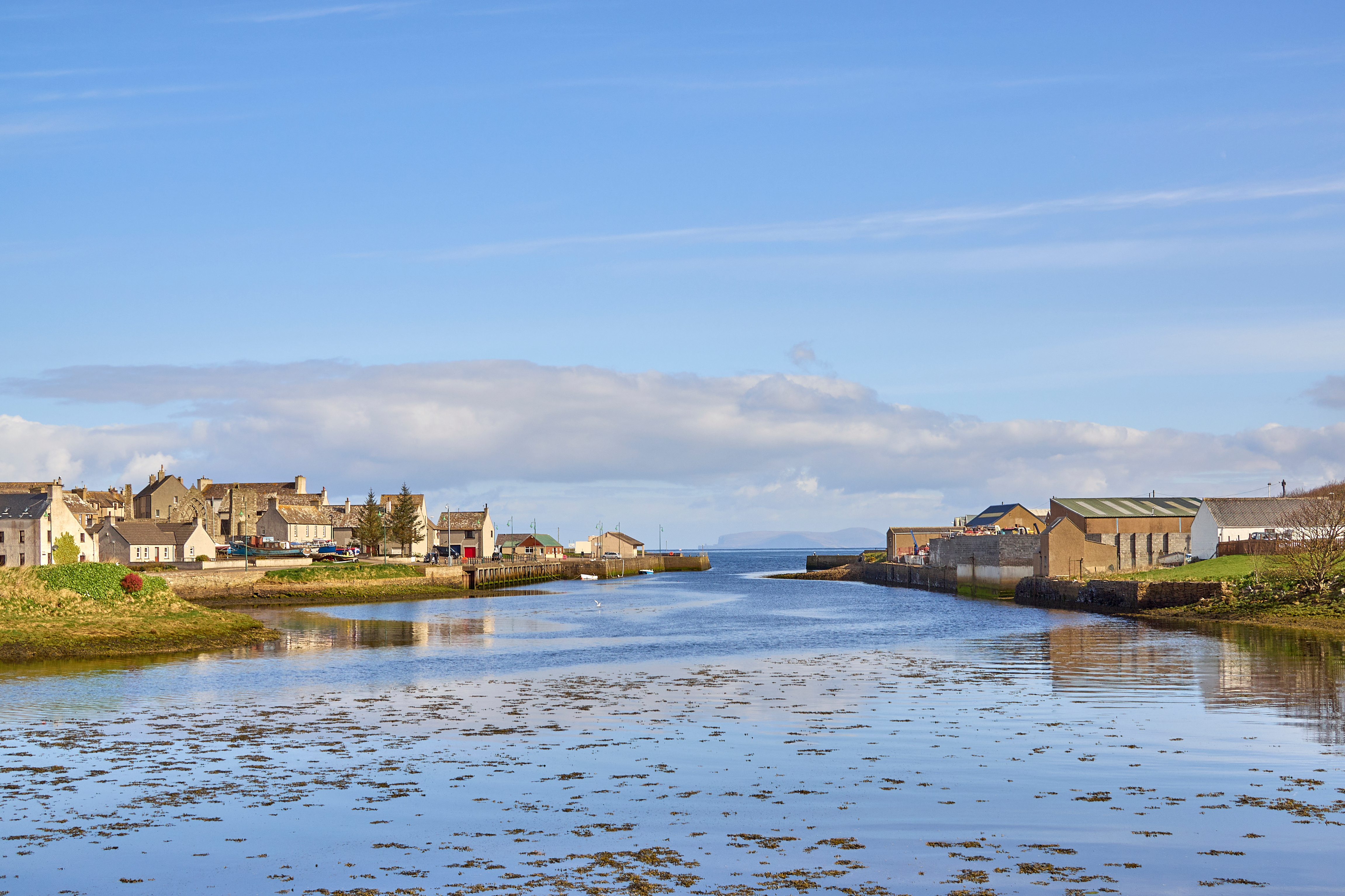 A quiet harbour scene with buildings along the water under a bright sky.