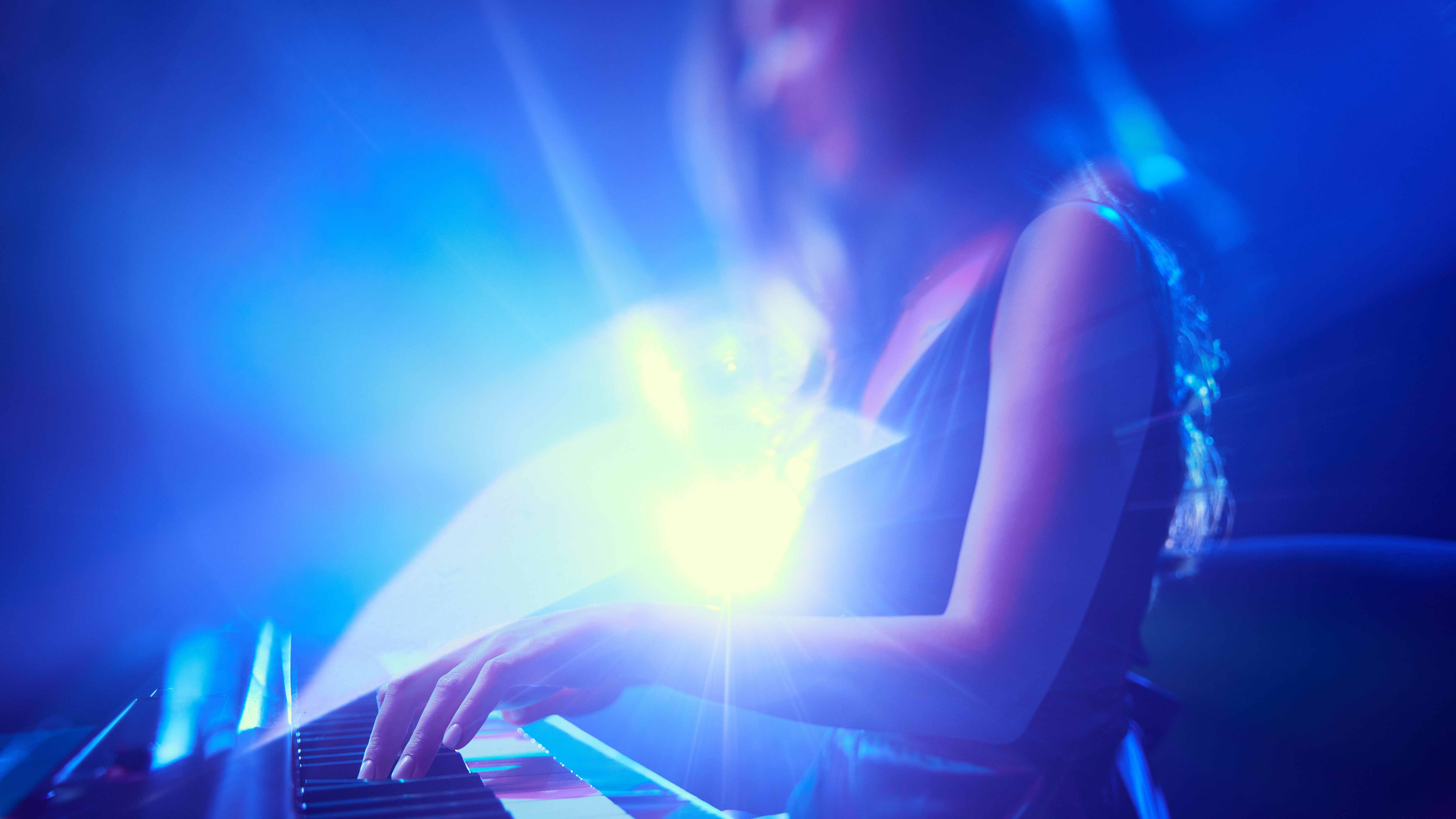 A person playing a keyboard onstage with bright blue stage lighting.