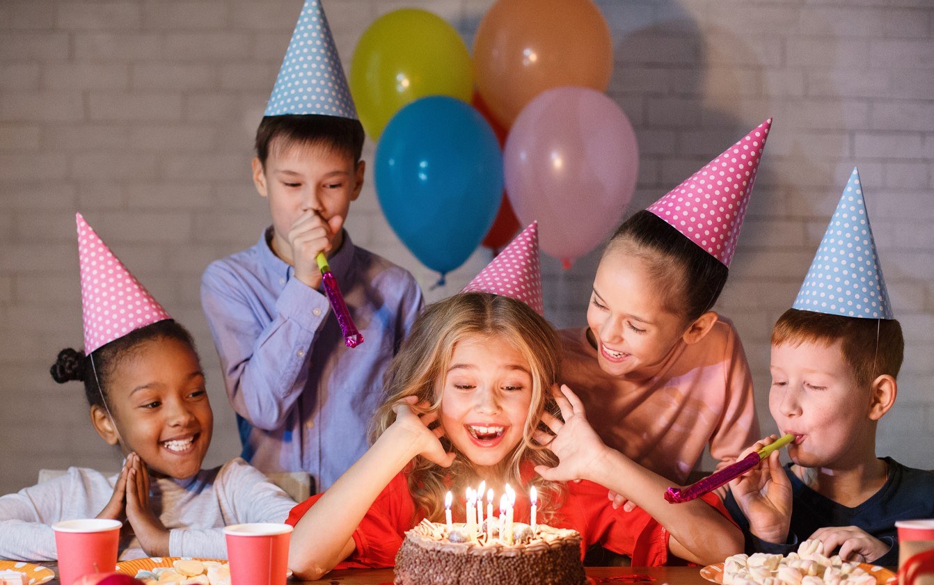 Children donning party hats gathered behind a birthday cake.
