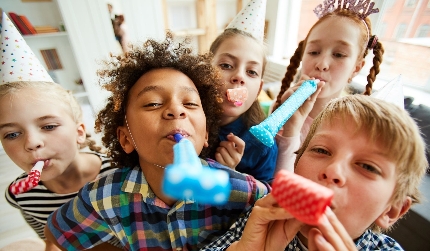 Children donning party hats blowing party hooters.