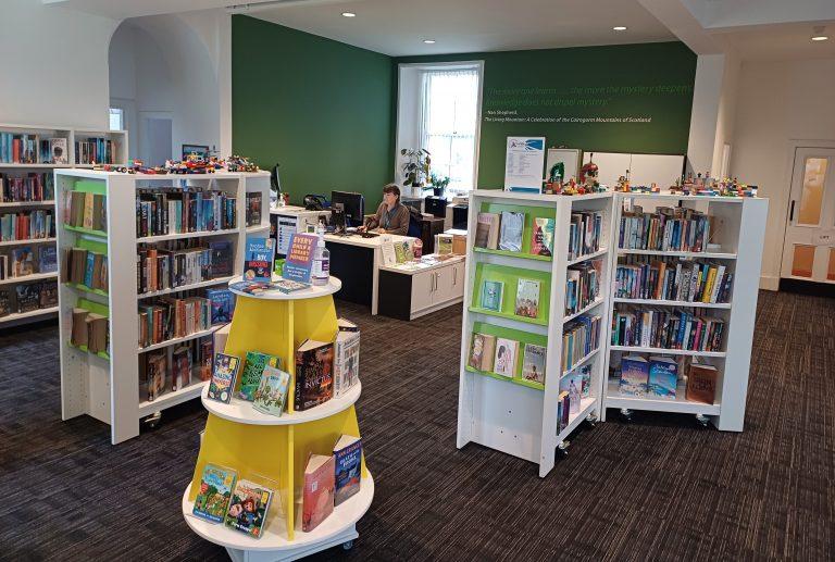 Interior of a library with bookshelves, a circular book display, and a person working at a desk.
