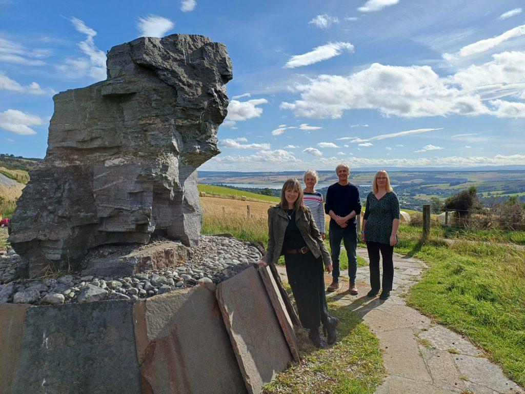 Four people beside a large rock formation in open countryside under a blue sky.