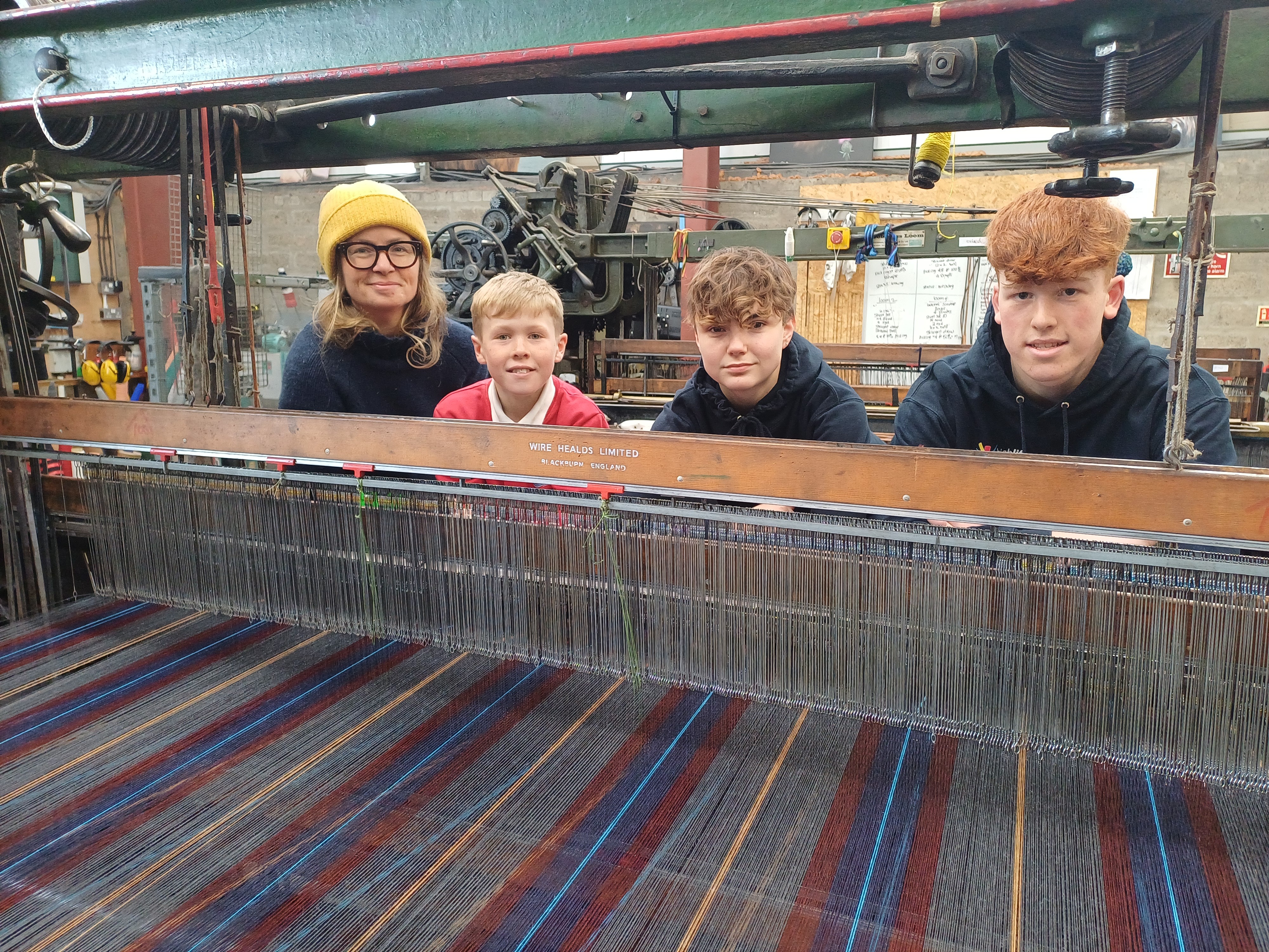 Clare Campbell of Prickly Thistle with Youth Pipe Band drummers Ollie Baker, Megan Fraser and Cameron Brown, standing behind a loom weaving the new tartan at Prickly Thistle's mill in Evanton.