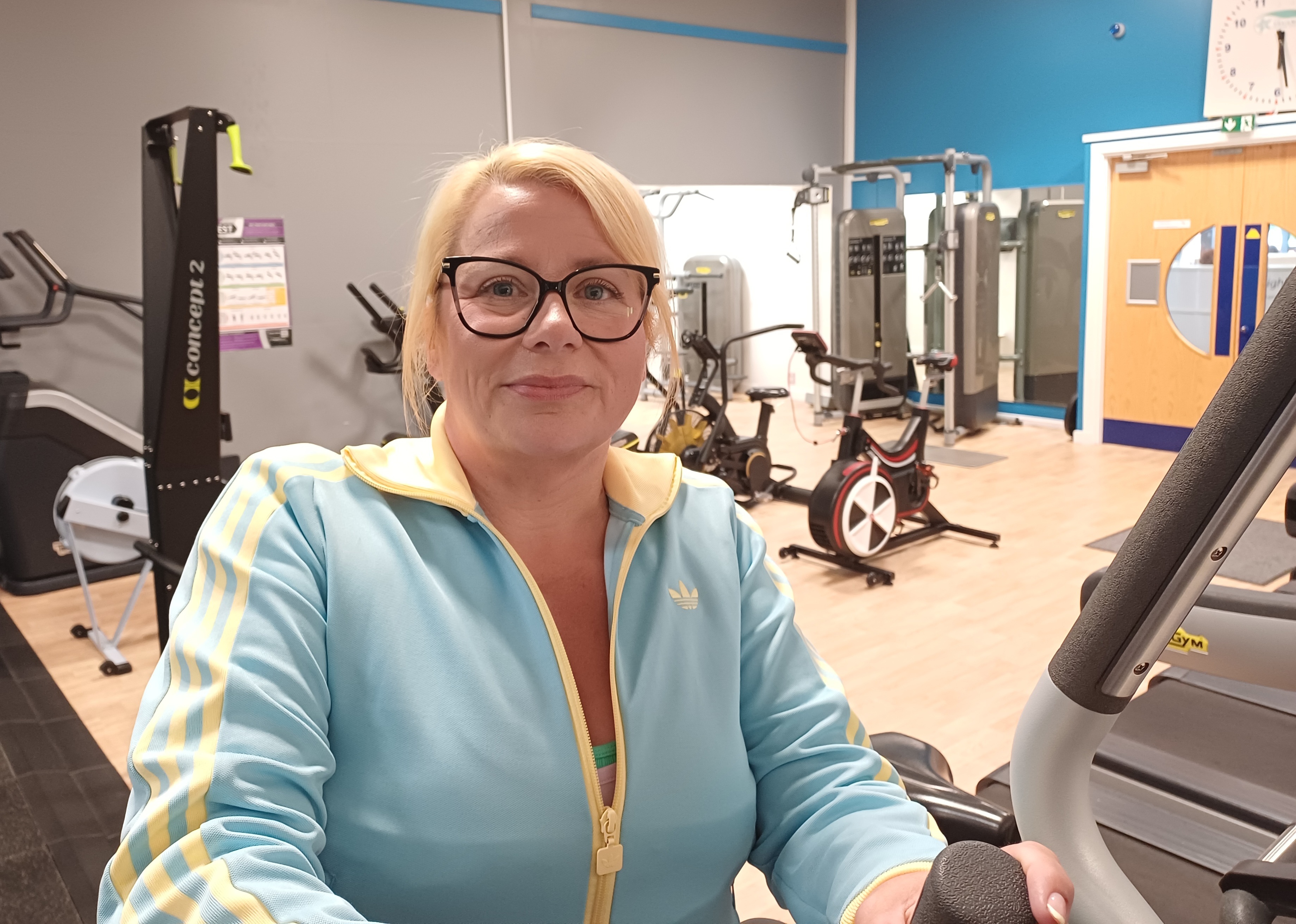 Denise smiling in the fitness suite at Craig Maclean Leisure Centre, surrounded by gym equipment.