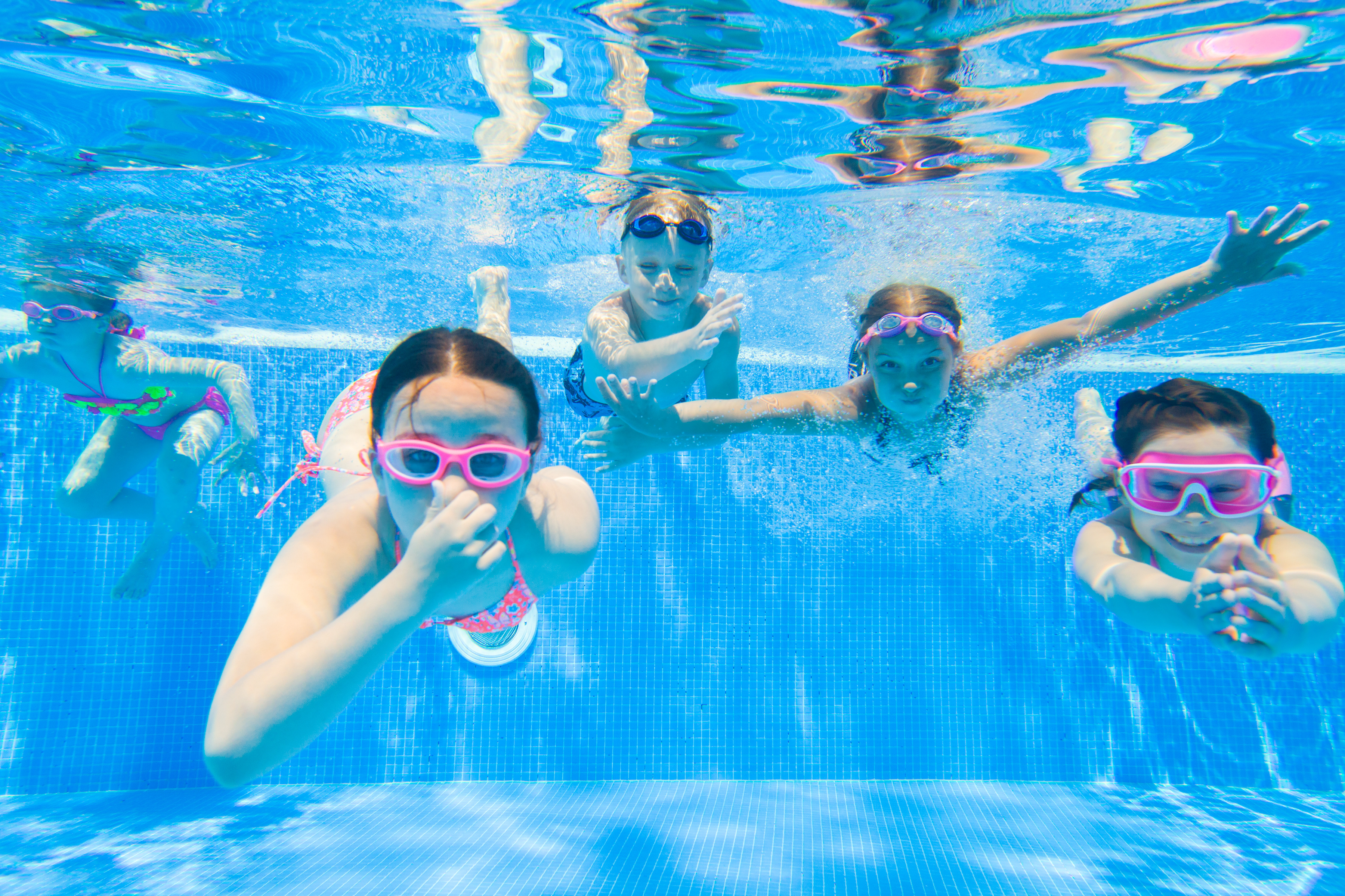 Children swimming underwater in a pool wearing goggles