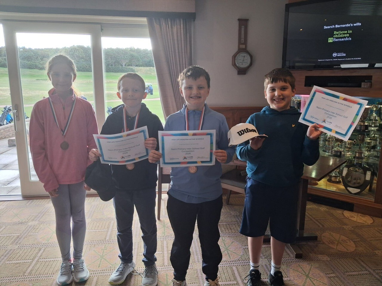 Four pupils holding certificates and medals in a golf clubhouse.