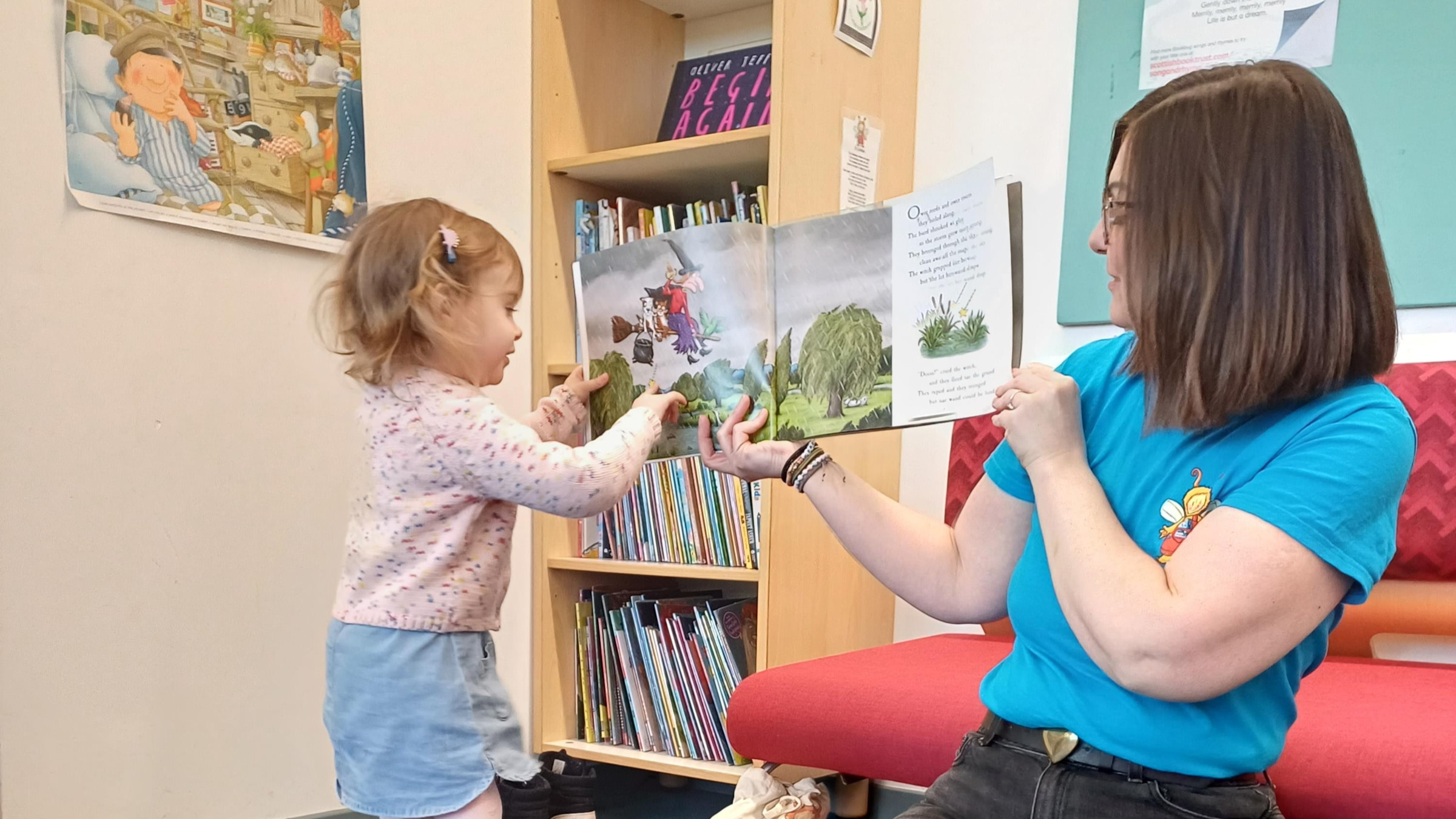 A library staff member holds open a picture book for a toddler, who reaches out to touch the page.