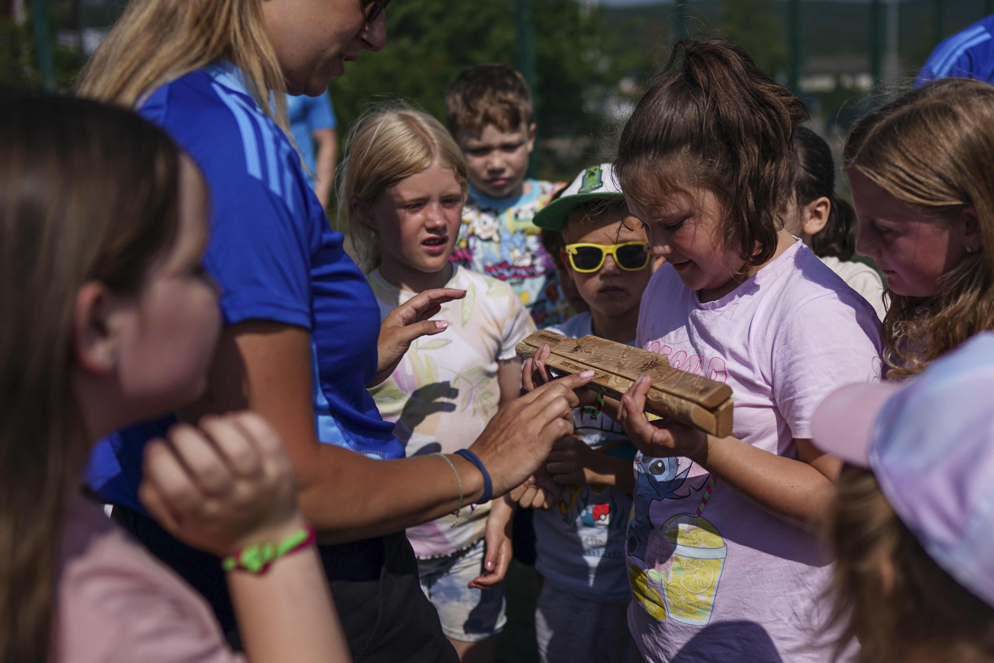 Children gathered round the King's Baton outdoors on a sunny day