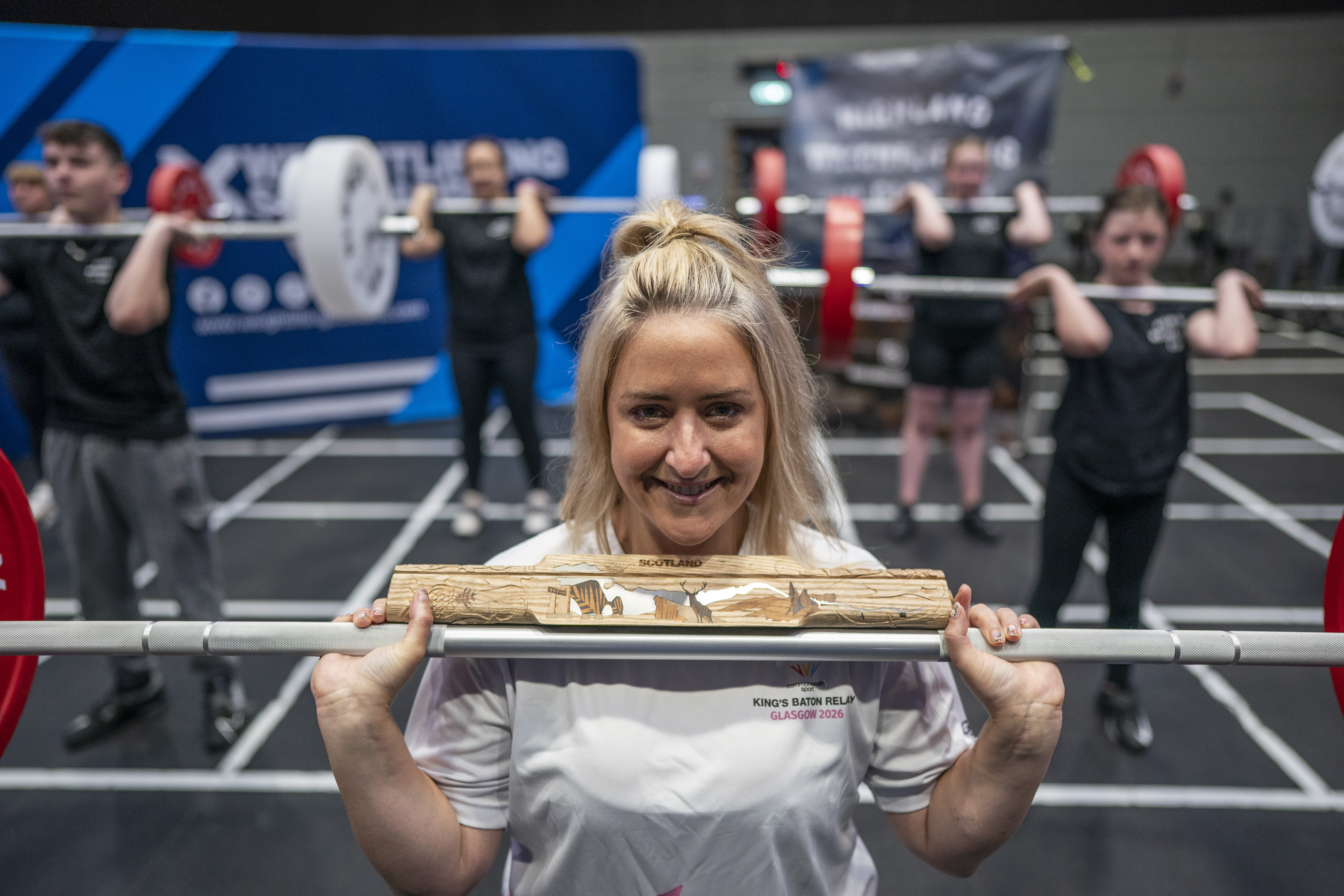 Weightlifter holding the King's Baton across a barbell in the gym