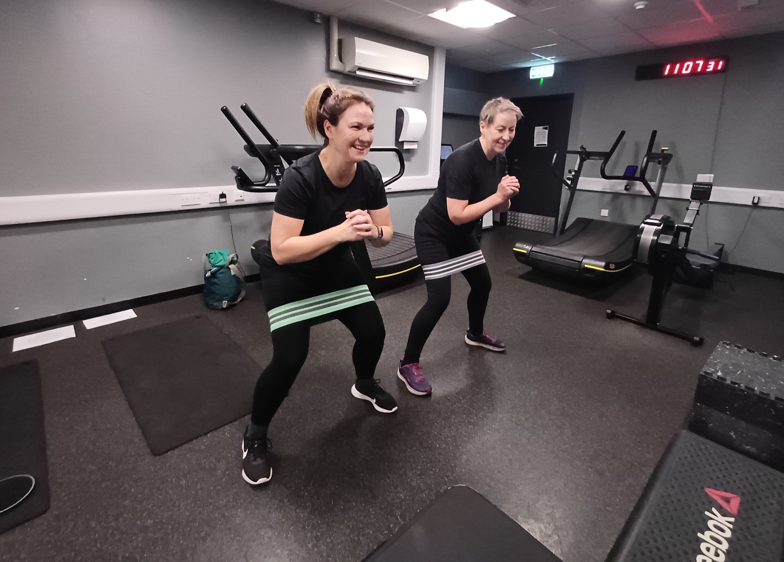 Two women perform resistance band squats during a cancer rehabilitation class at Inverness Leisure