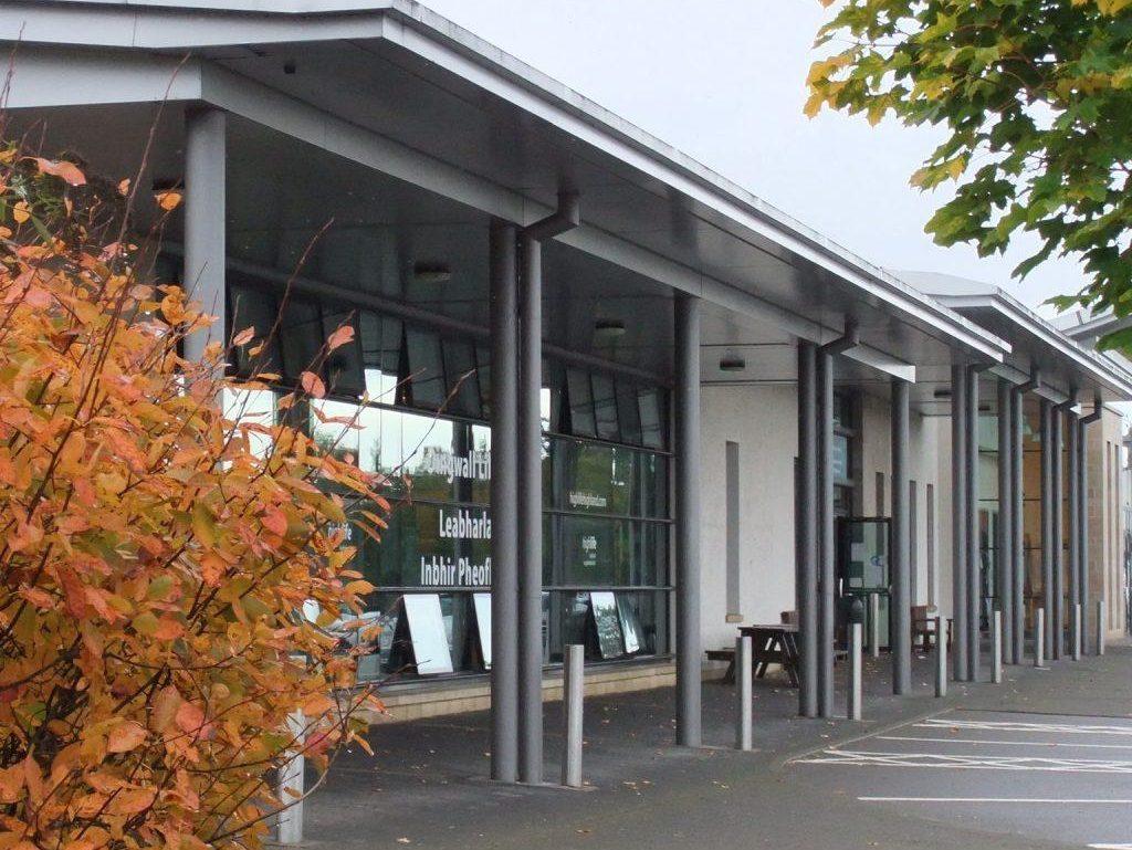 Exterior of Dingwall Library, a modern building with large glass windows, a slanted roof, and autumn trees surrounding the entrance.