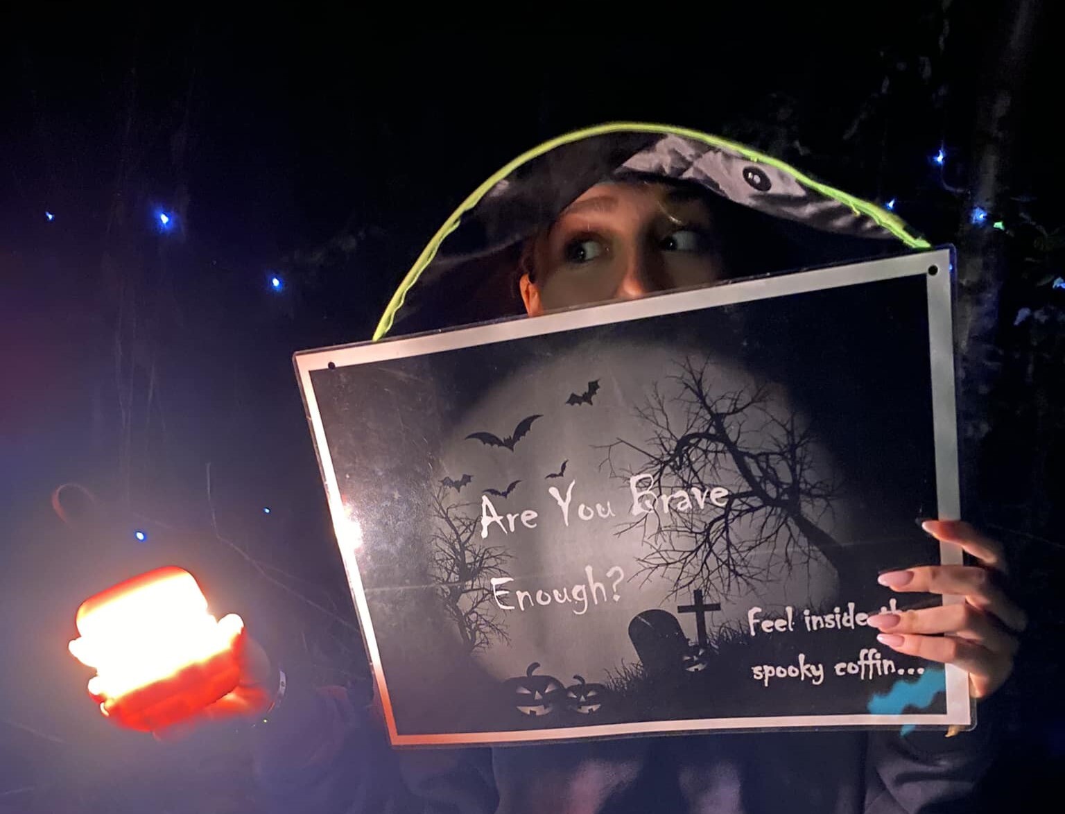 A lady in a witches hat holding a sign and a lantern