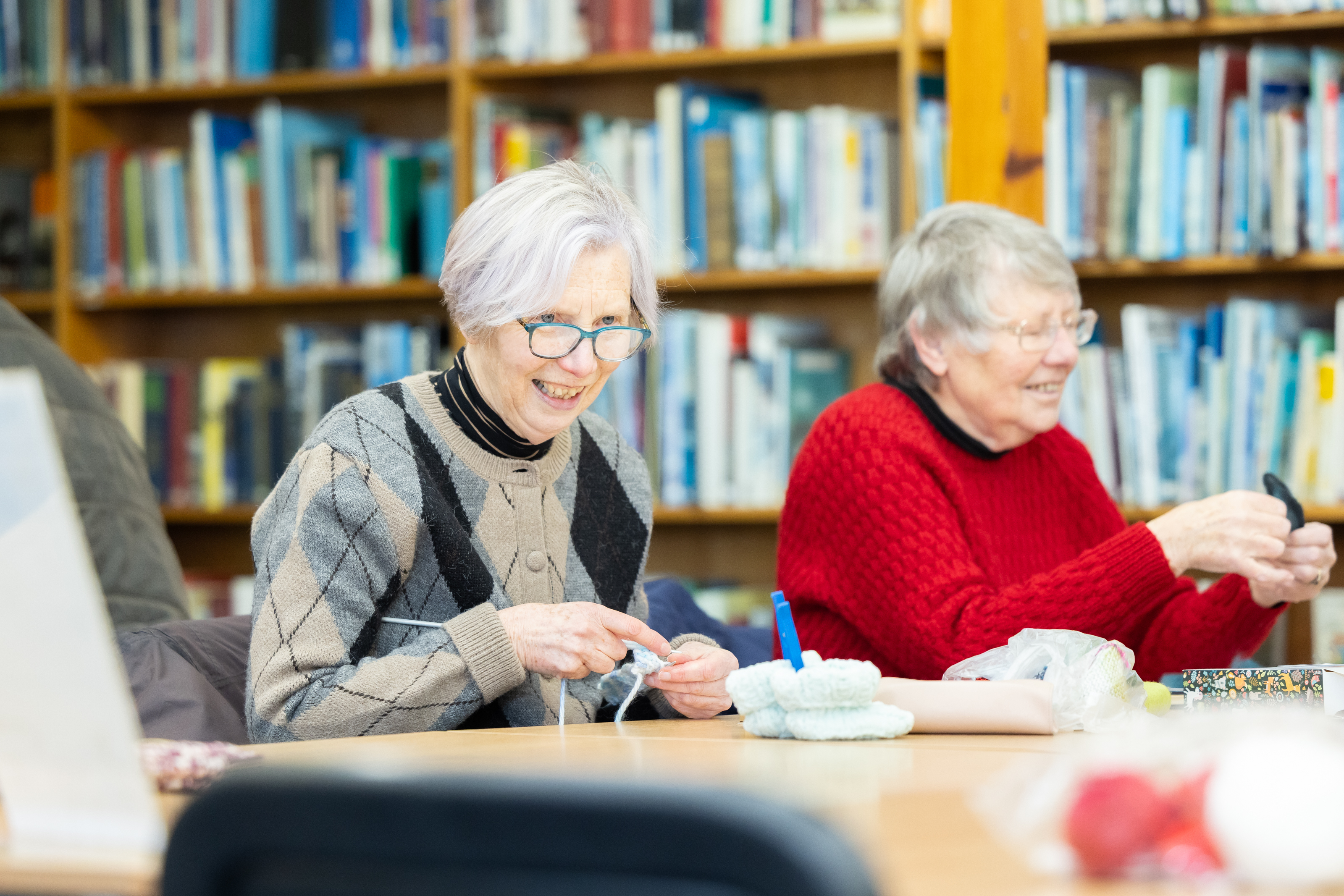 Woman laughing while knitting with library staff member nearby
