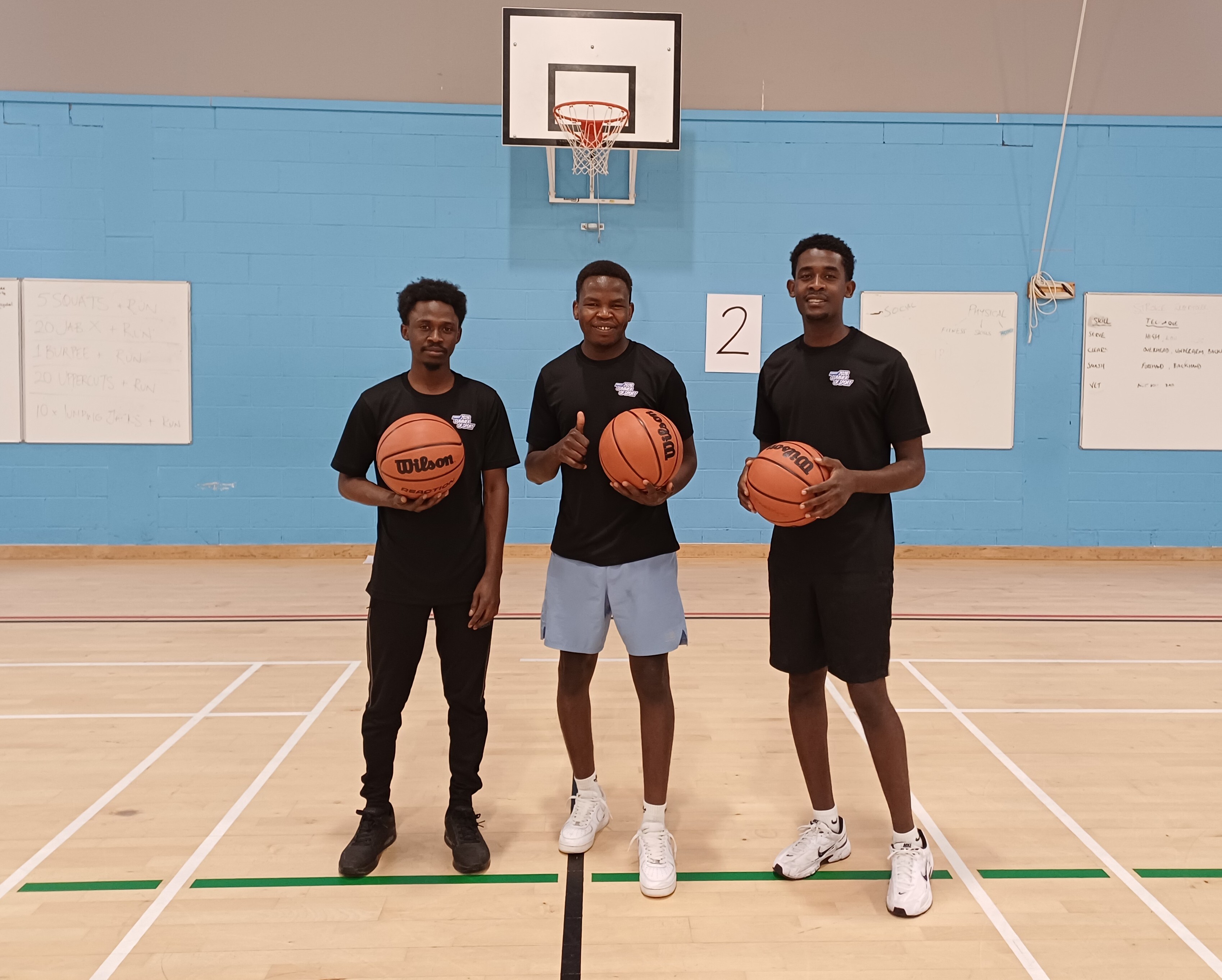 Three young men holding basketballs in the sports hall