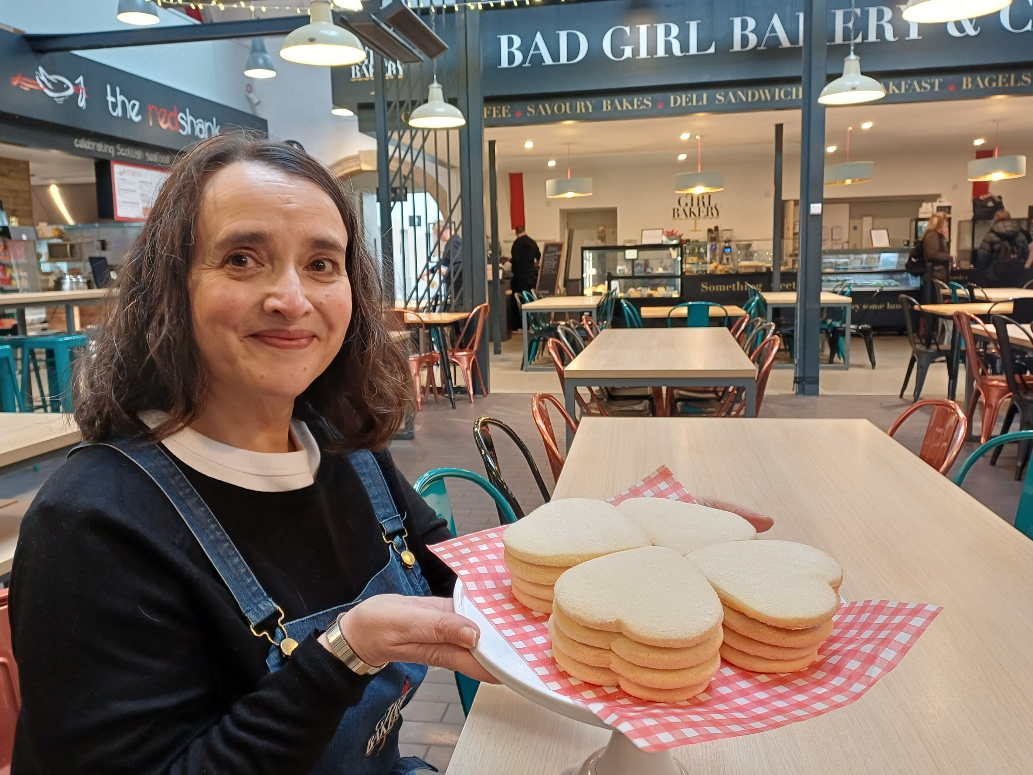 Woman in a denim apron holding a cake stand of heart-shaped shortbread in a café