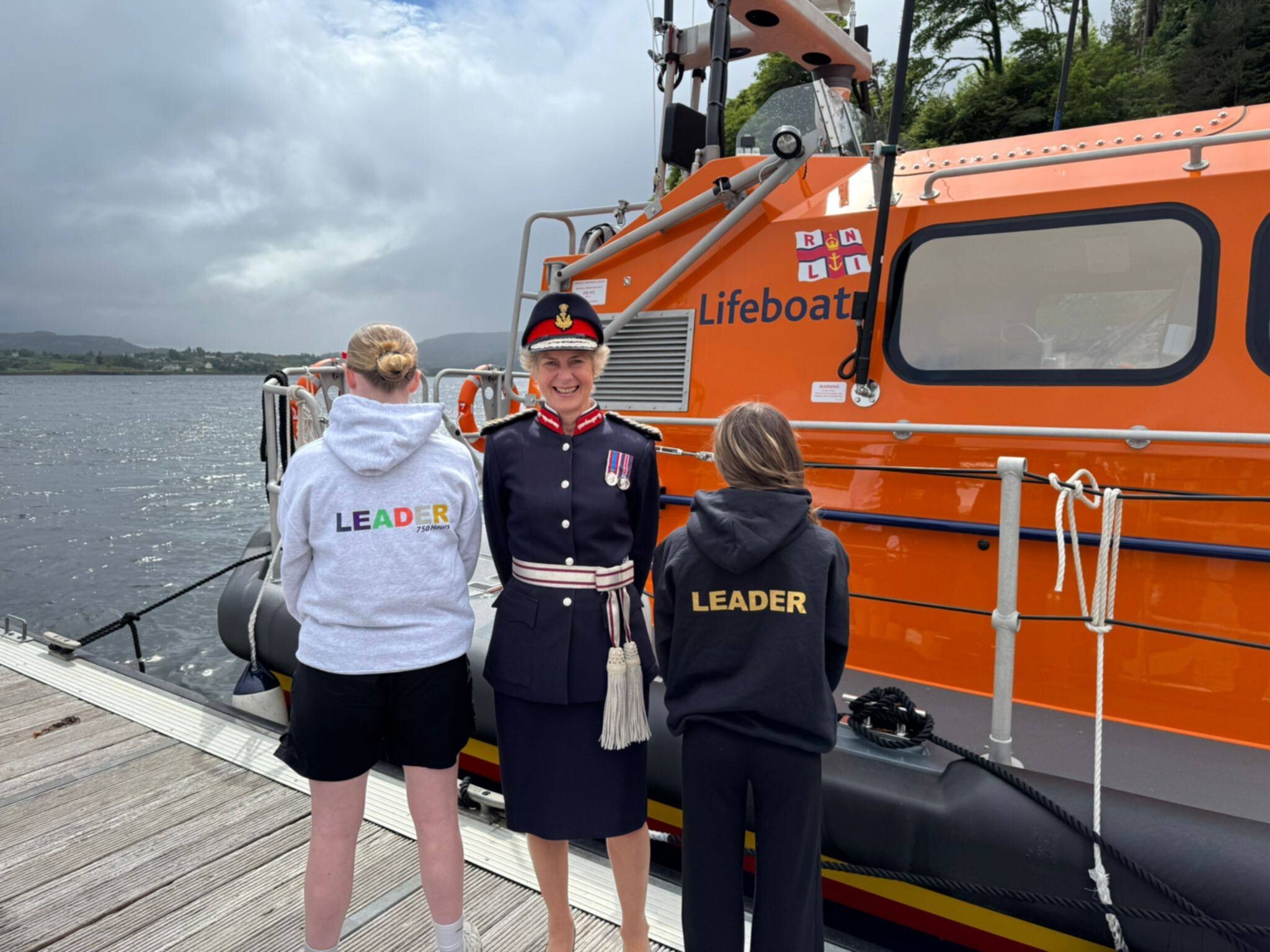 Two pupils wearing "Leader" hoodies stand with Lord Lieutenant Joanie Whiteford beside the Portree RNLI lifeboat