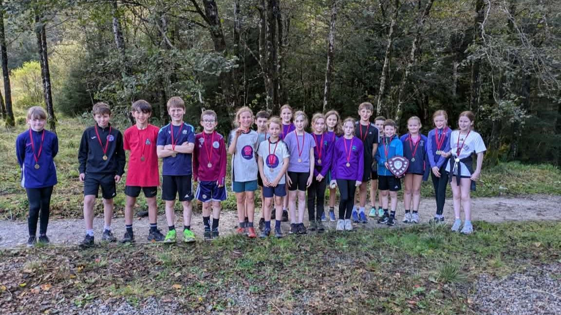 Group of primary school pupils wearing medals on a forest path, one holding a shield.