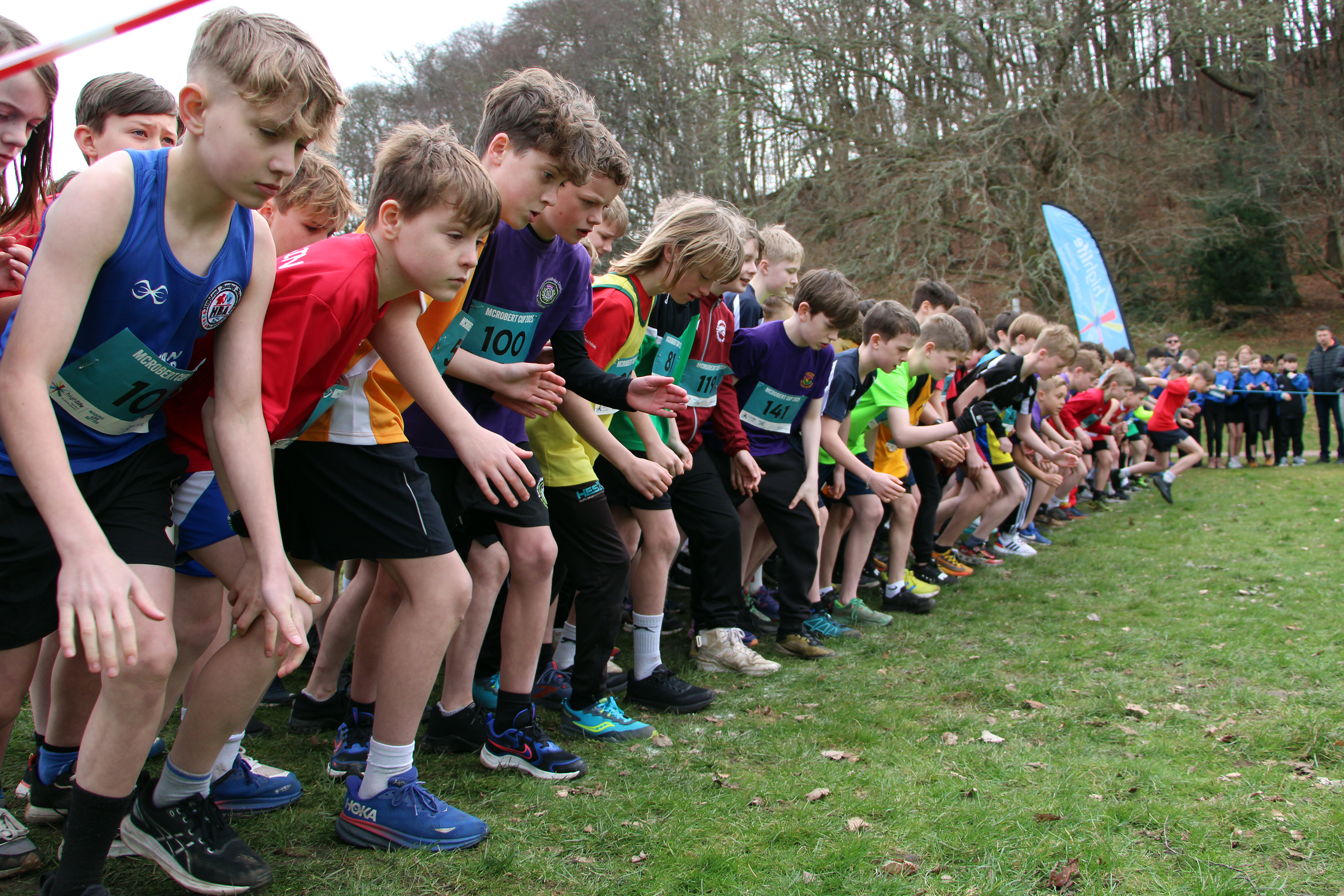 A group of primary school boys lined up ready to start a running race in a park.