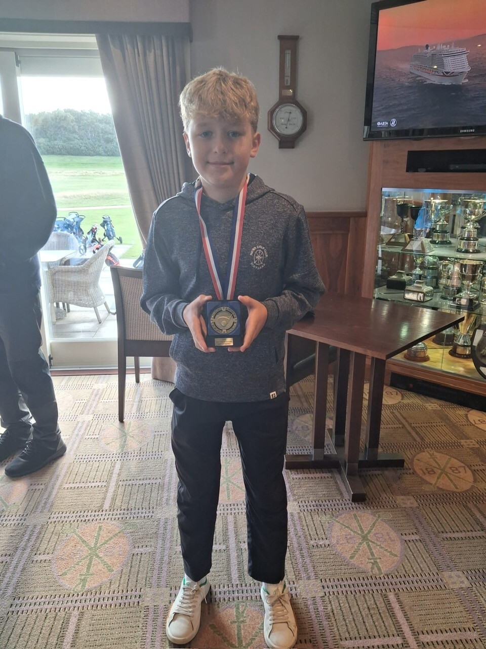Young golfer holding a medal and a plaque.