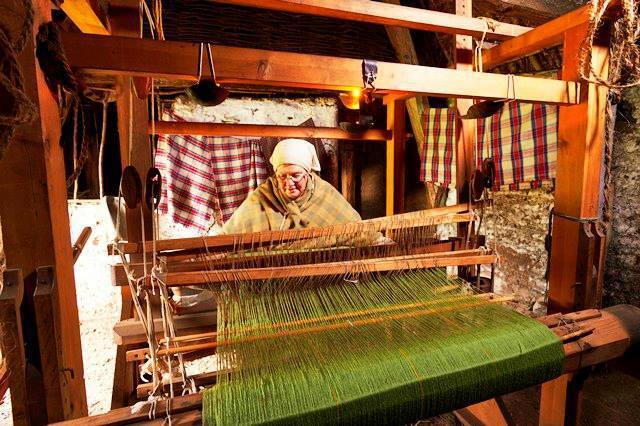 A woman dressed in old fashioned clothing sitting behind a large weaving loom.