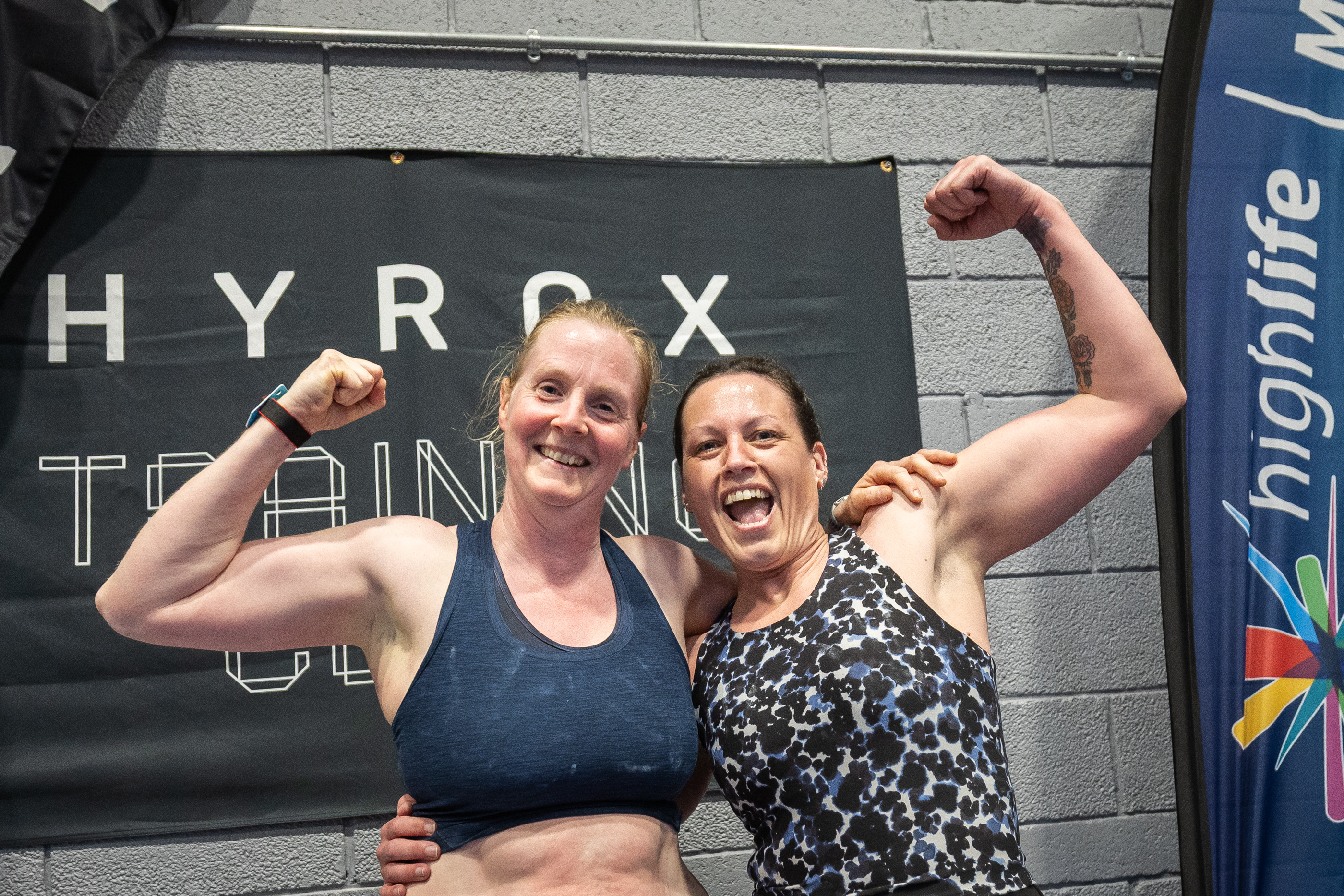 Two women smiling and flexing their arms after a training session