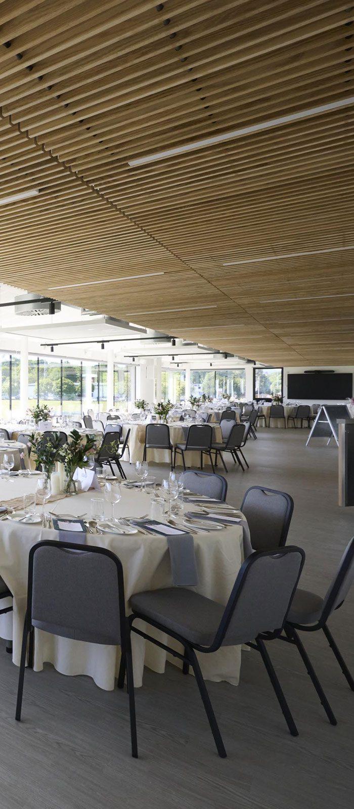 The space features a spacious, well-lit room adorned with floor-to-ceiling windows along one exterior wall. Arranged with round tables and comfortable chairs, it creates an inviting atmosphere, making it ideal for weddings or formal dining events.