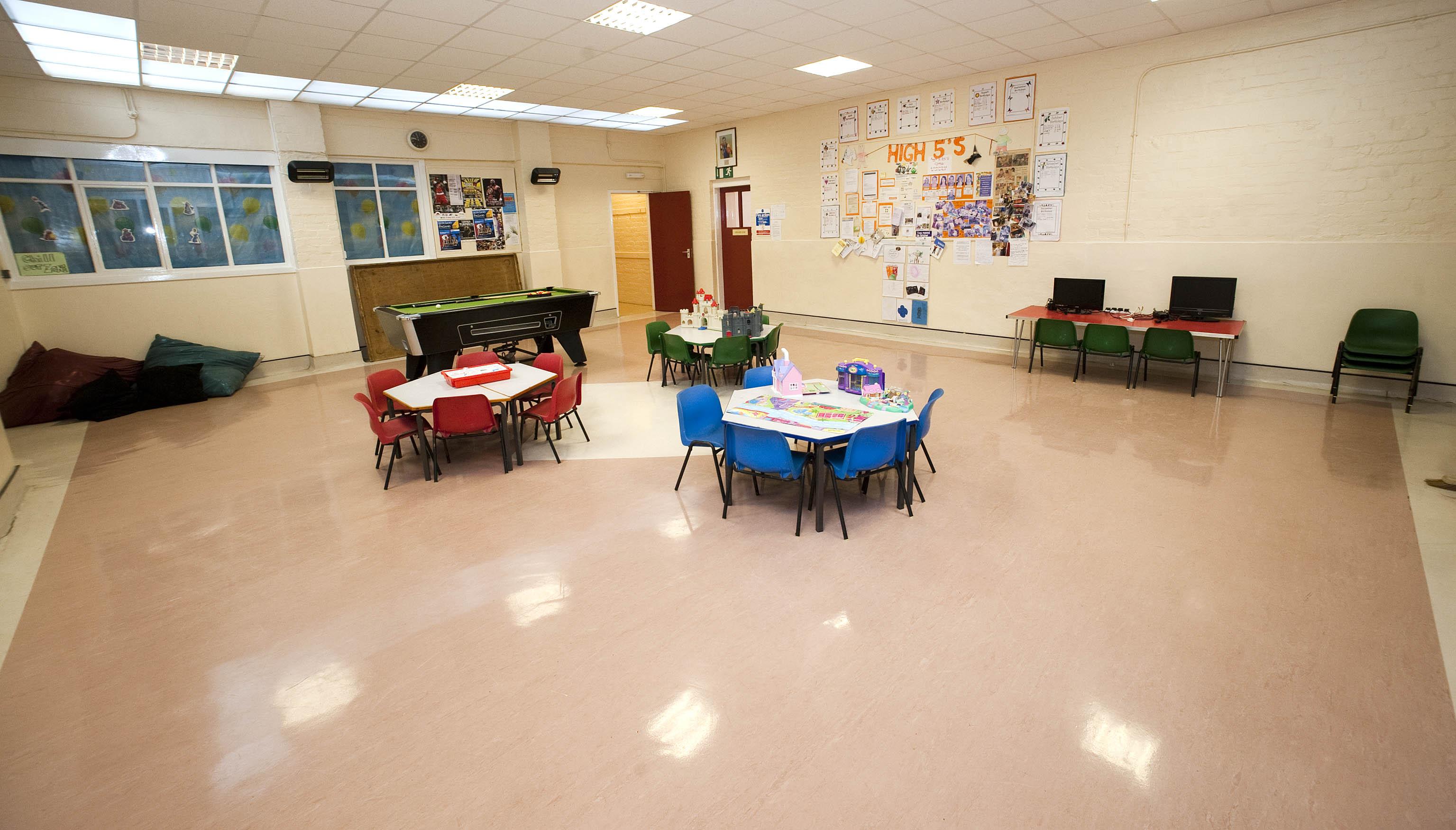 A spacious room featuring linoleum flooring, arranged with small tables and chairs suitable for children, along with a pool table.