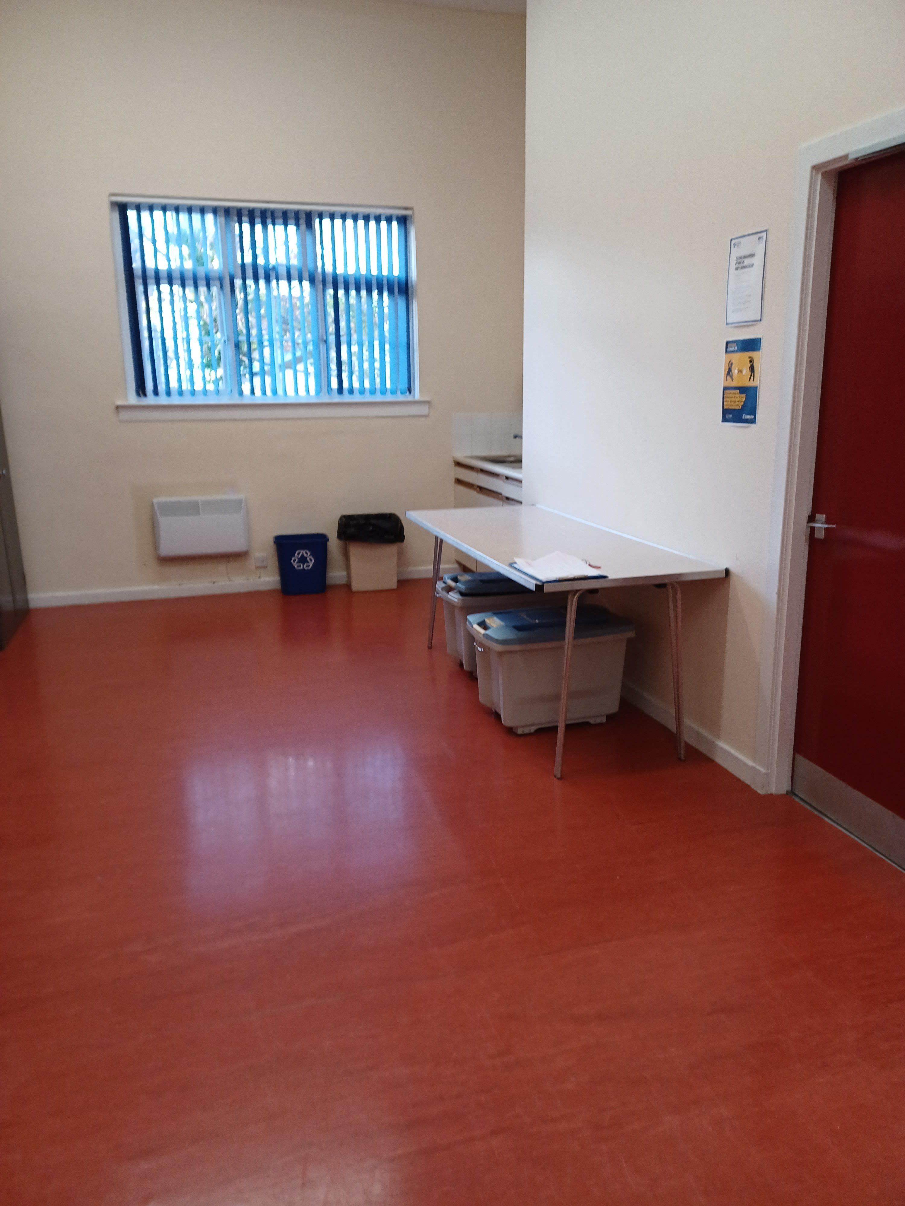 A brightly lit room featuring linoleum flooring, equipped with a sink in one corner and a table positioned against the wall.