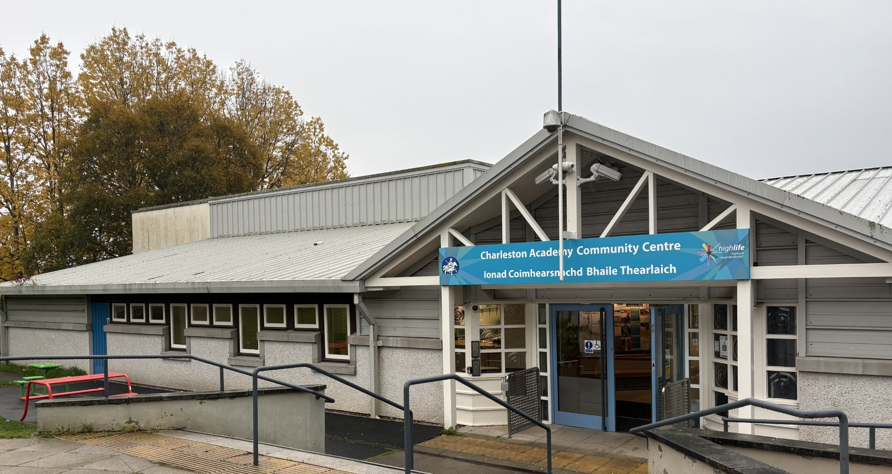 The building is a single-storey structure featuring steps that lead down to the main entrance, complete with handrails for safety. It boasts ample windows that allow natural sunlight to illuminate the facility throughout the day.