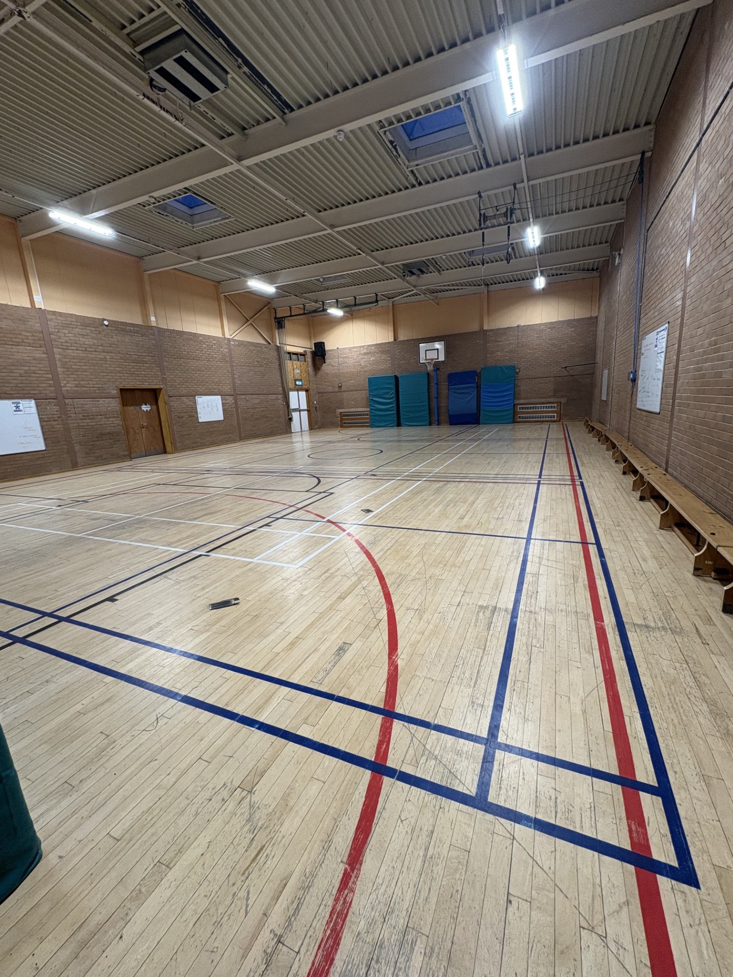 A spacious hall featuring badminton court and basketball floor markings, complete with basketball hoops positioned at each end.