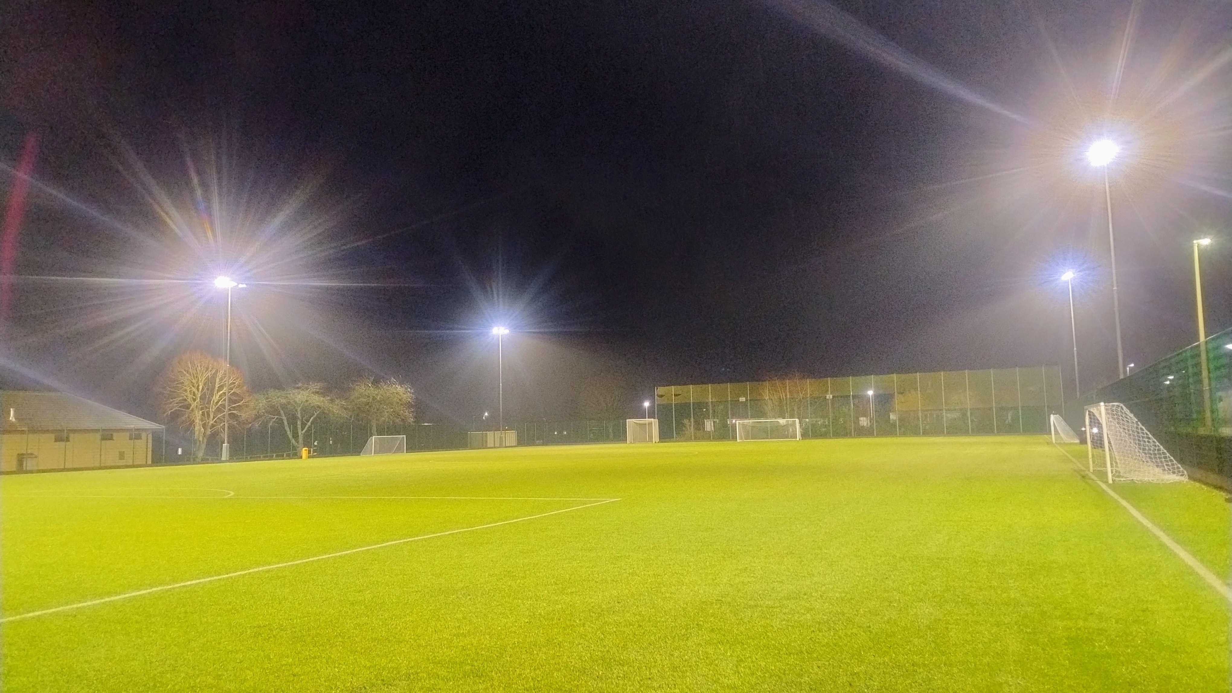 Astro turf marked with pitch lines, featuring multiple goals and ample lighting.