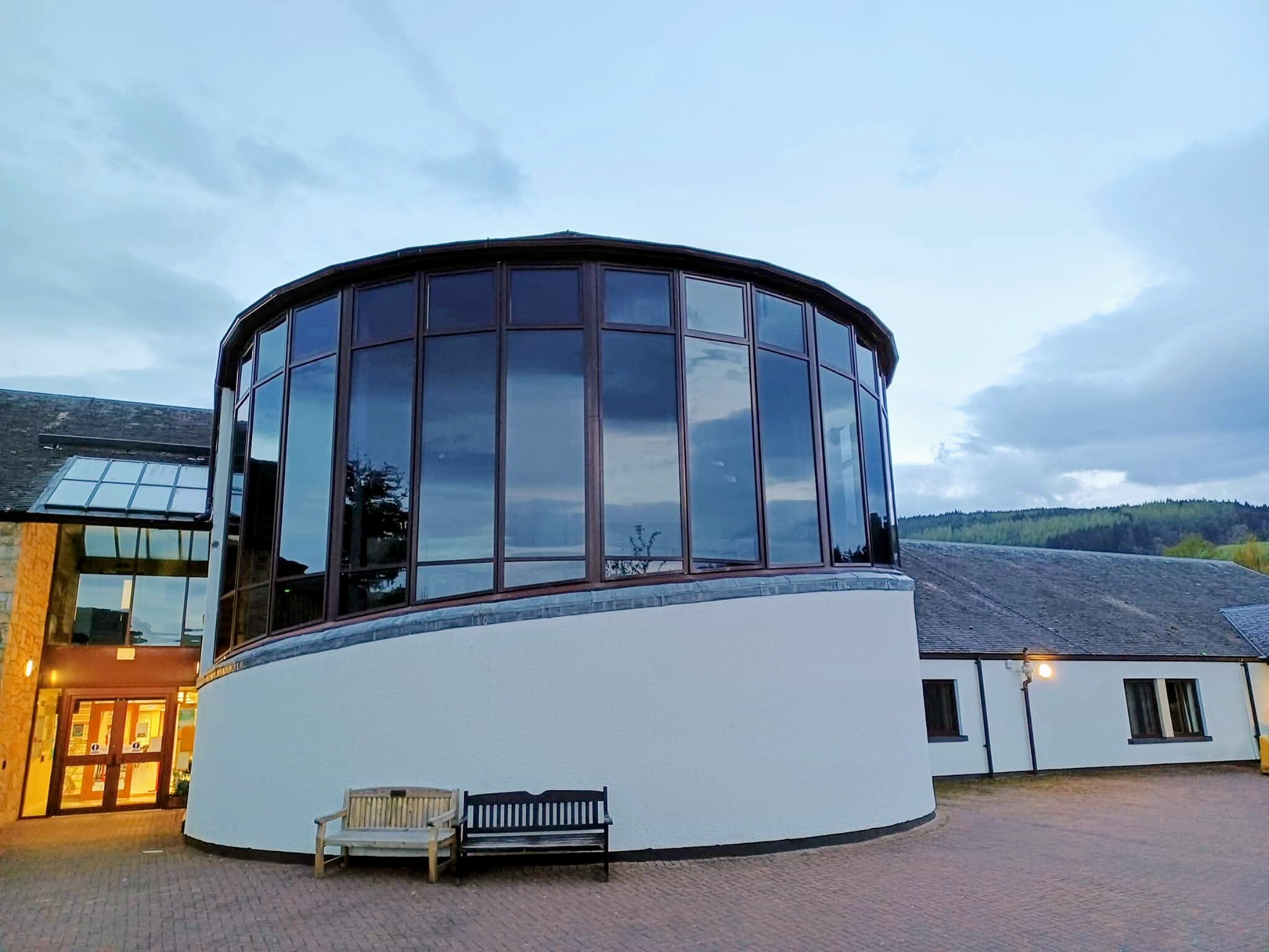 The structure is a contemporary building featuring a circular front room adorned with expansive full-length windows that offer panoramic views.