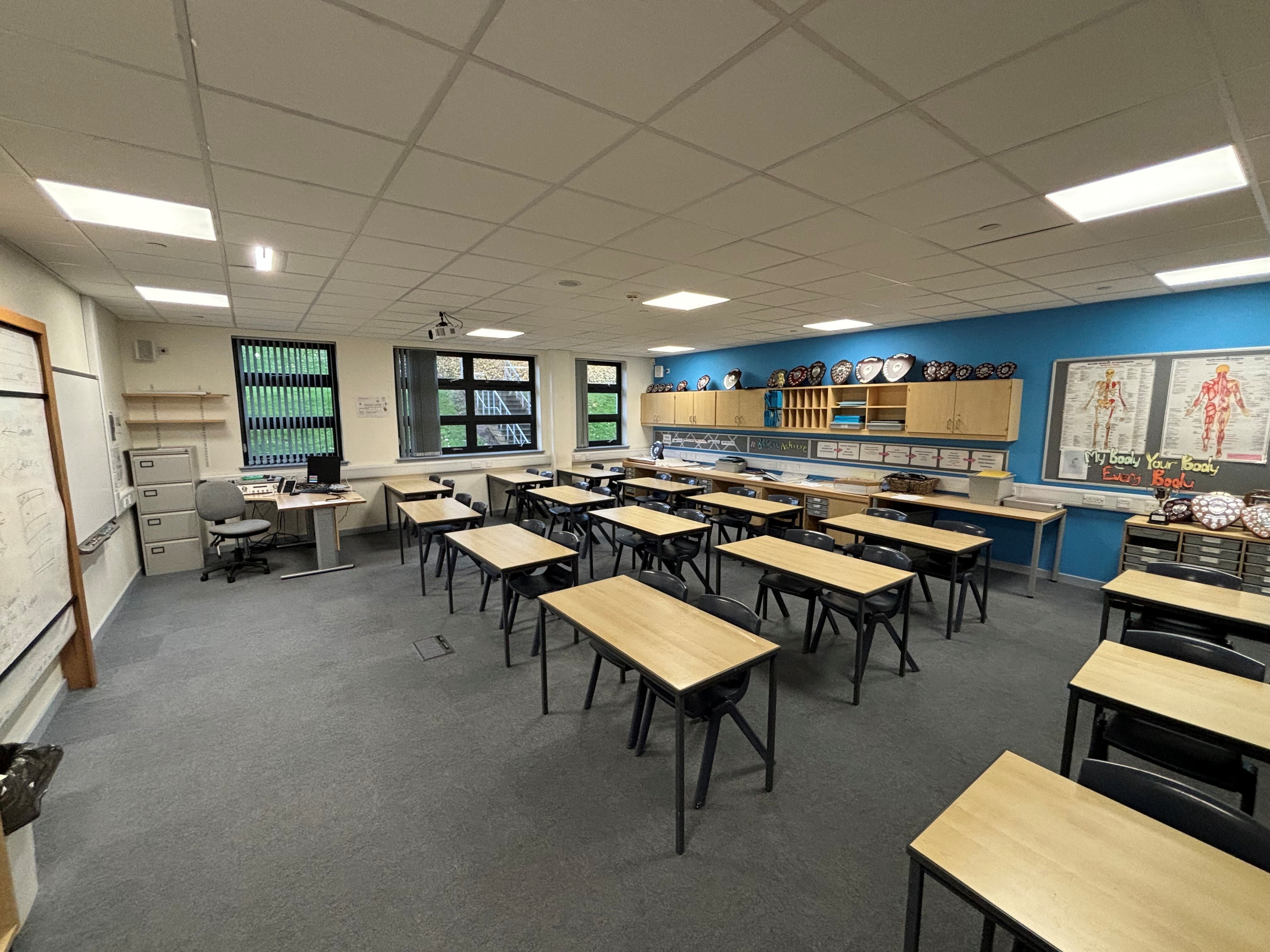 The room is arranged in a classroom format, featuring individual tables and a whiteboard positioned on the wall in front of the desks.