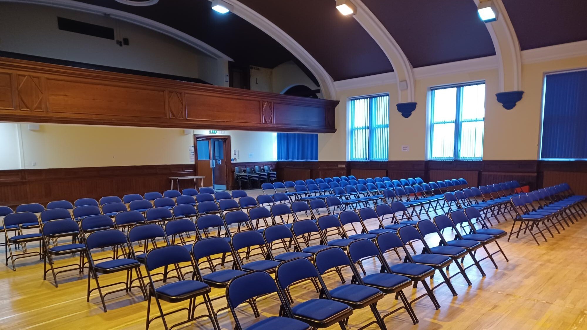 Large hall with approx 120 chairs set up. Seated balcony above main area for viewing stage.