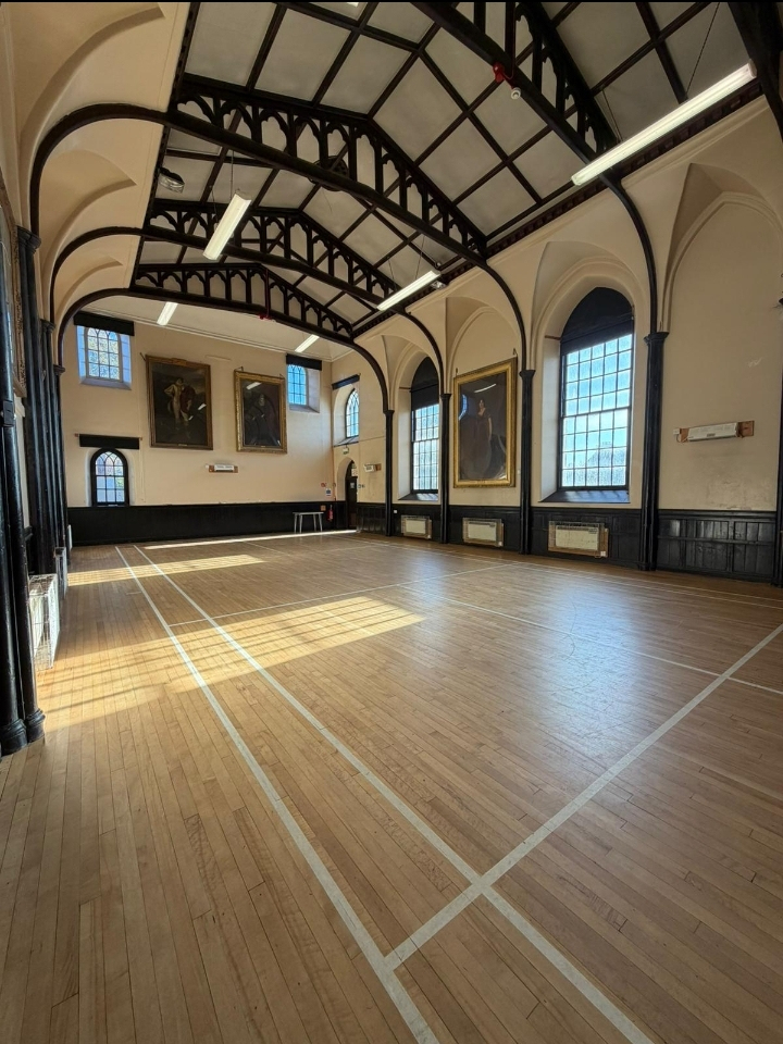 An impressive hall boasts a stunning arched ceiling and a badminton court flooring. Expansive windows allow for ample natural light to illuminate the space.
