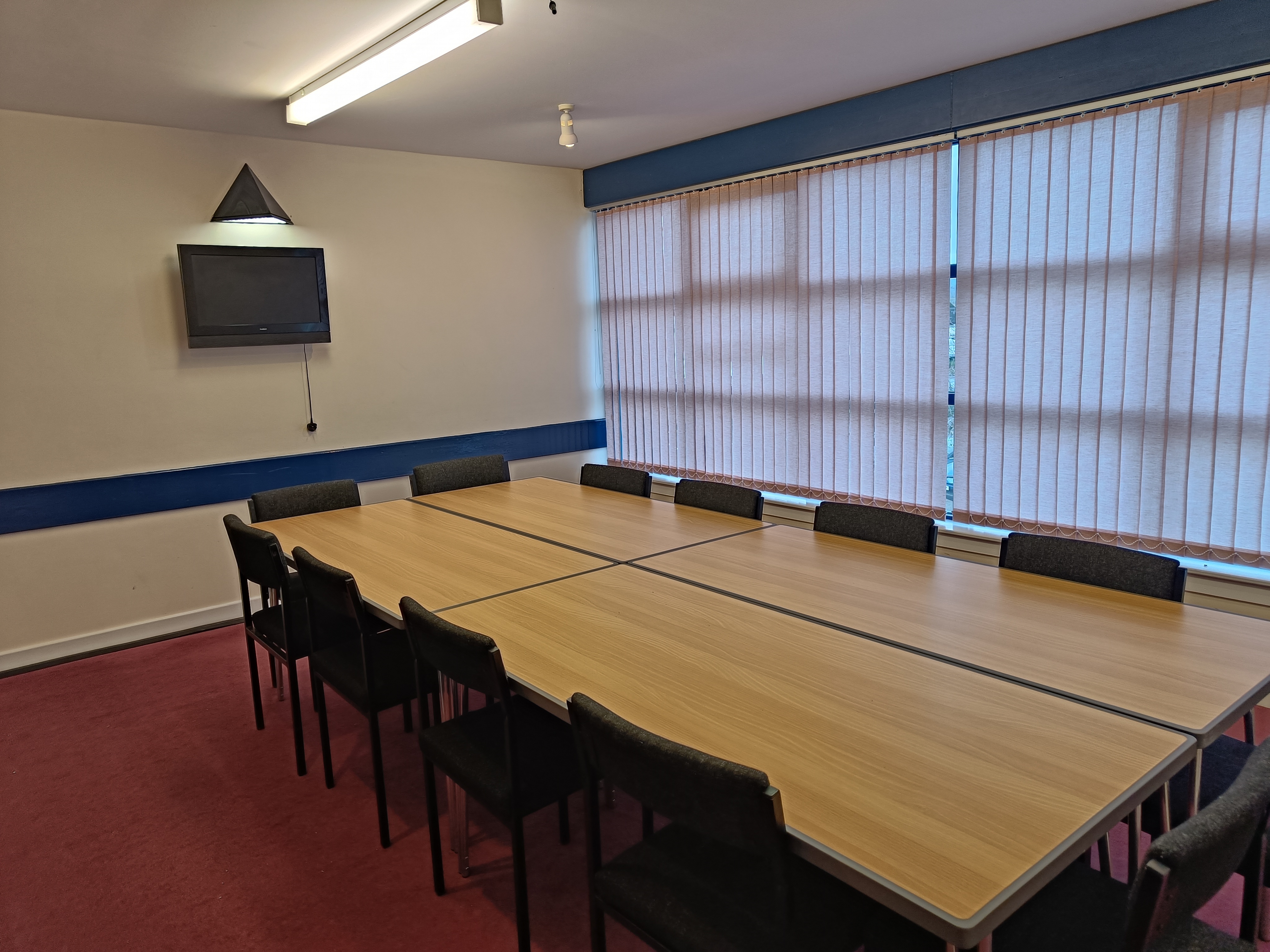 The room features a large meeting table at its center, surrounded by chairs, with a television mounted on the wall at one end.